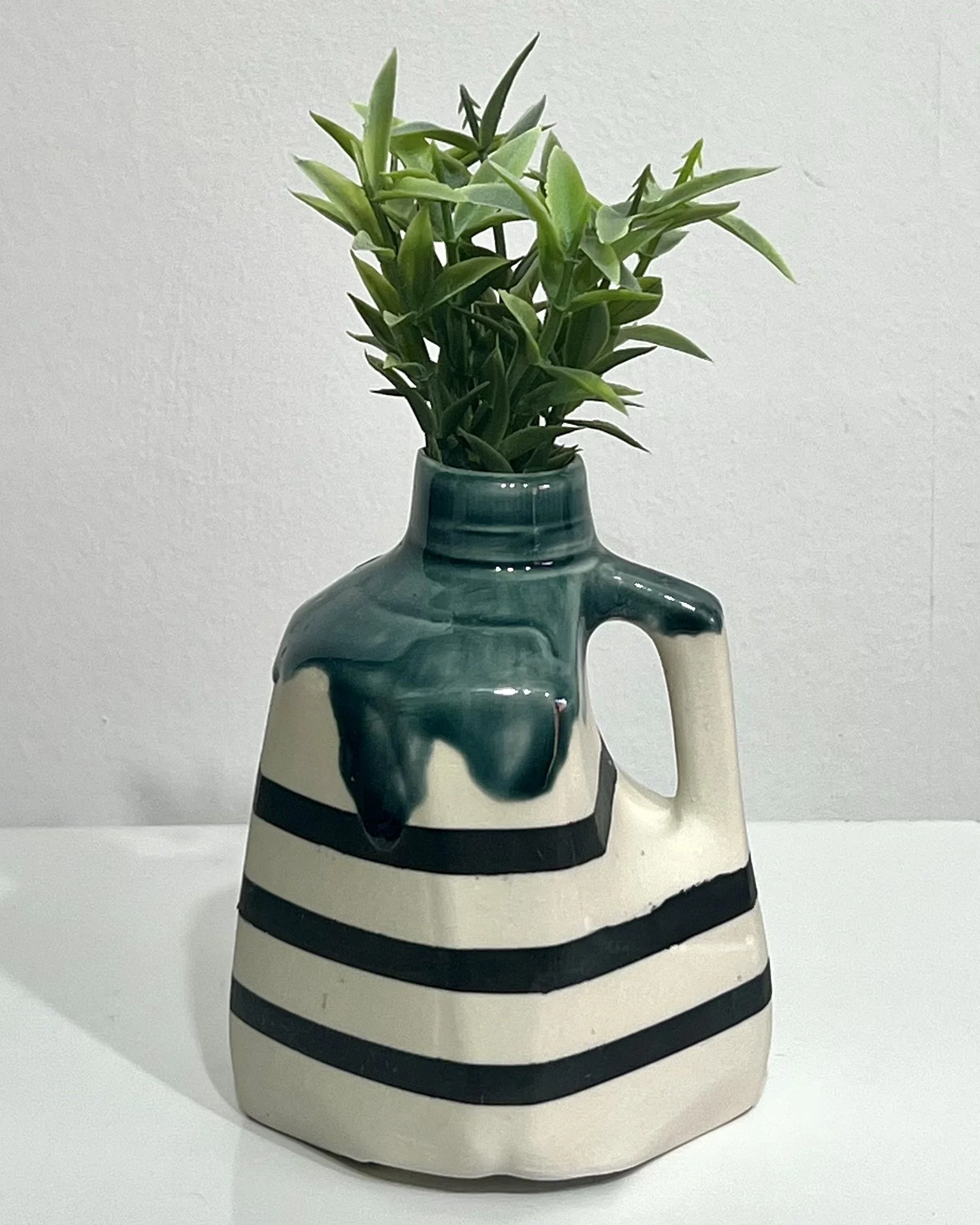 Handmade black and white striped porcelain milk jug No. 26.142 styled with green botanical stems, featuring a glossy teal-green neck and graphic horizontal stripes.