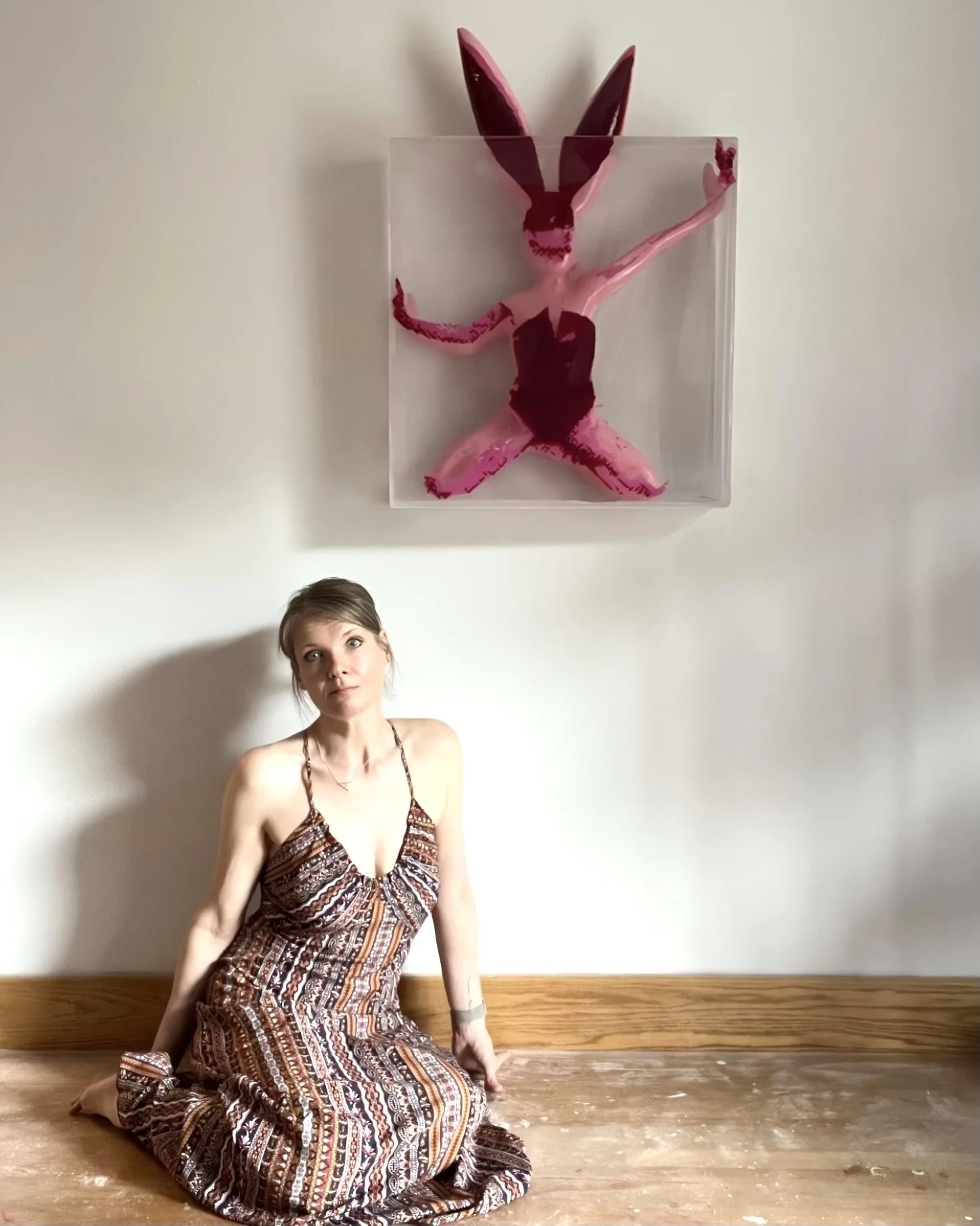 Alissa Van Atta seated beneath her resin sculpture “Wait for Me, I Think I’m Worth It,” showing scale and installation context