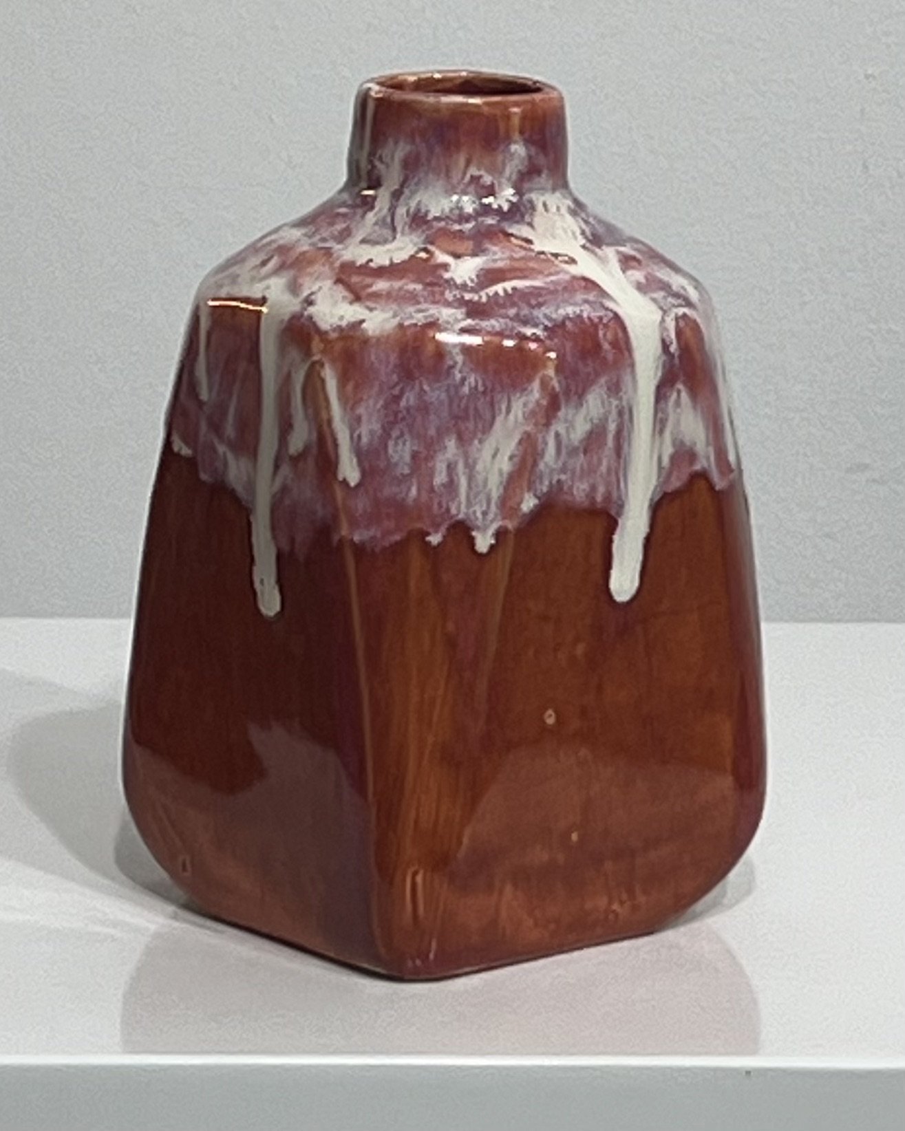 Side view of sculptural burgundy ceramic milk jug with cream glaze drips