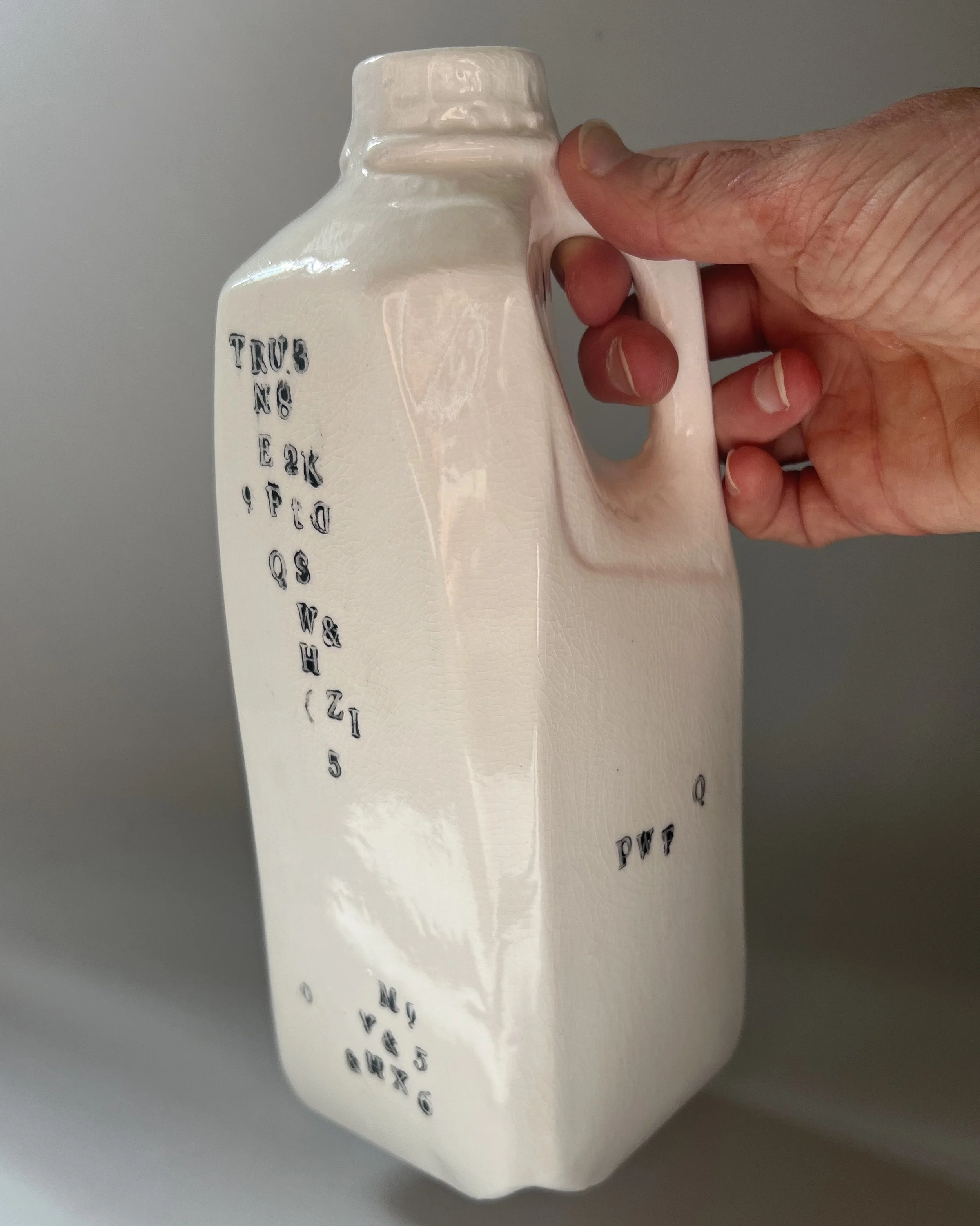 Hand holding a tall contemporary porcelain milk jug to show scale and proportions.