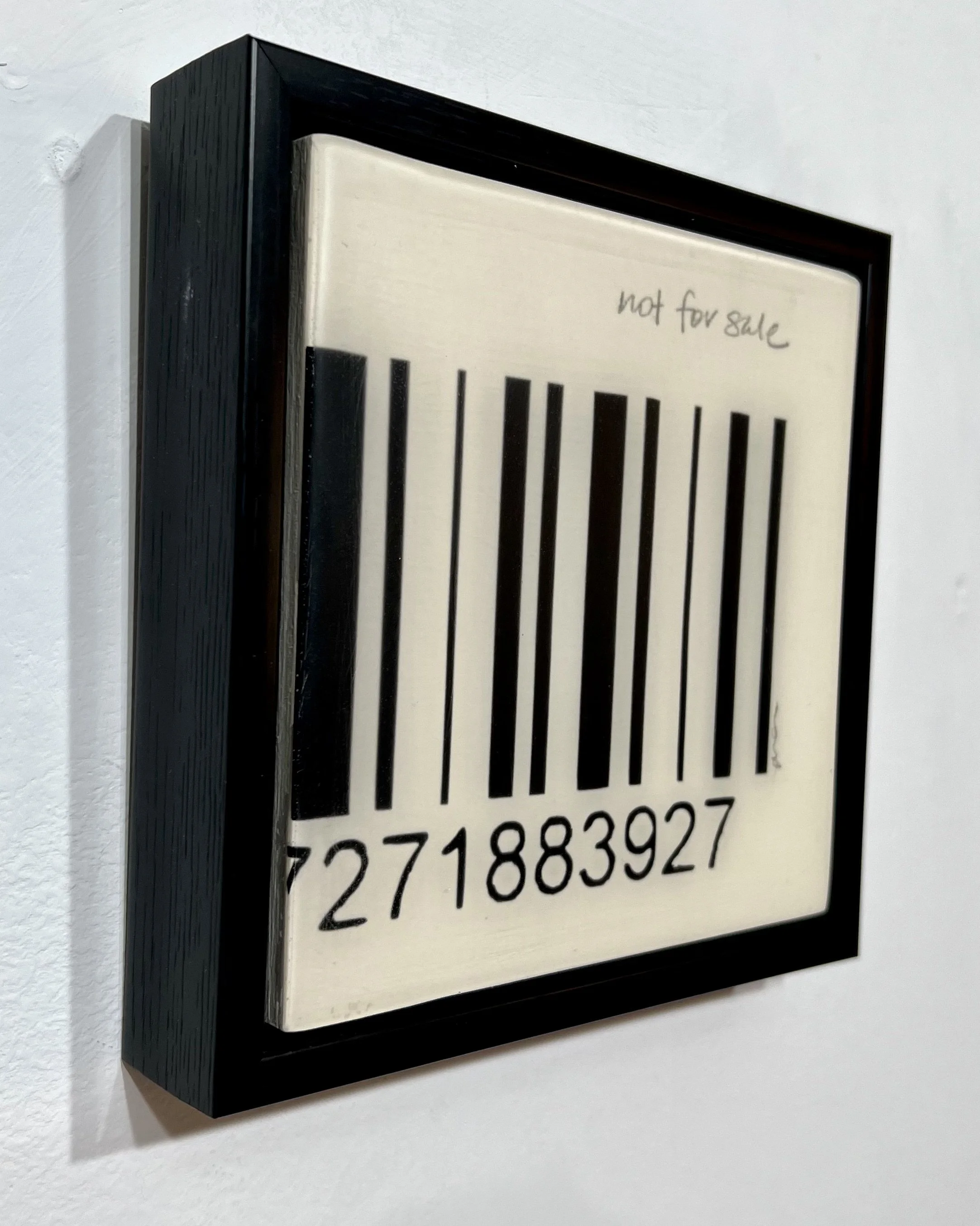 Angled view of Not for Sale, an original 6 by 6 inch resin and acrylic barcode collage on wood, displayed in a black frame by Alissa Van Atta.