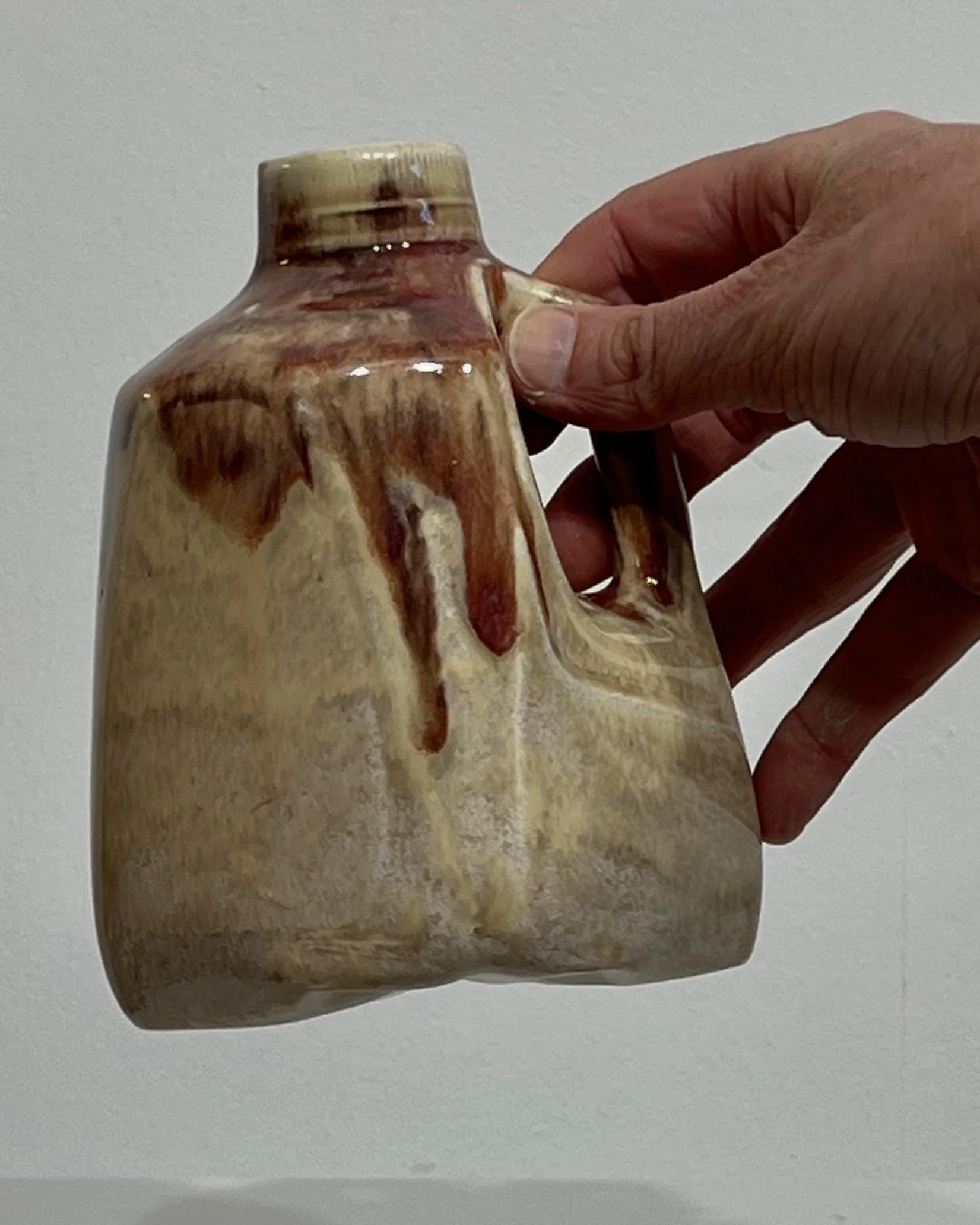 Small handmade cream and burgundy porcelain milk jug held in hand for scale