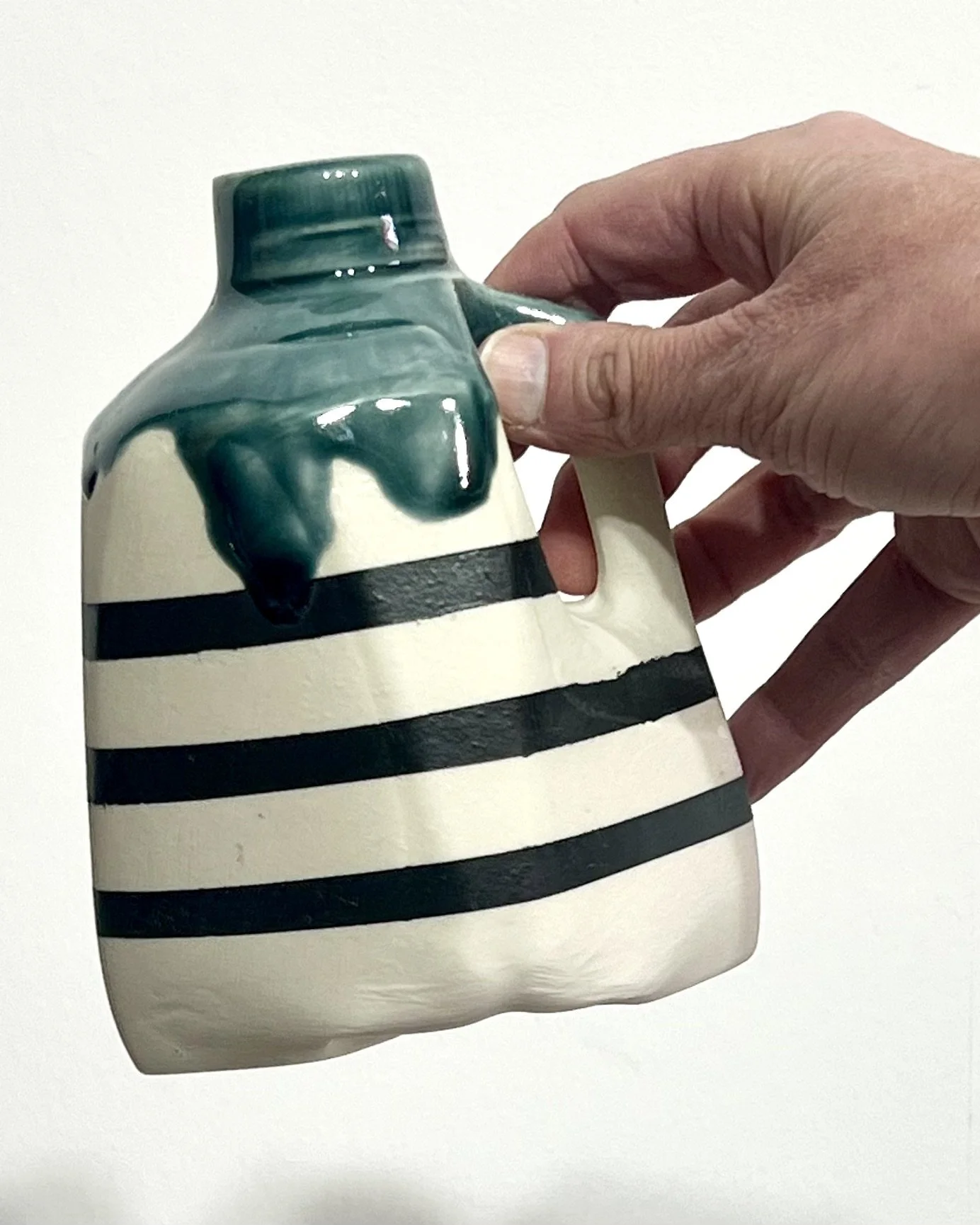 Hand holding striped porcelain milk jug No. 26.142 by Alissa Van Atta to demonstrate the ceramic vessel's compact size and proportions.