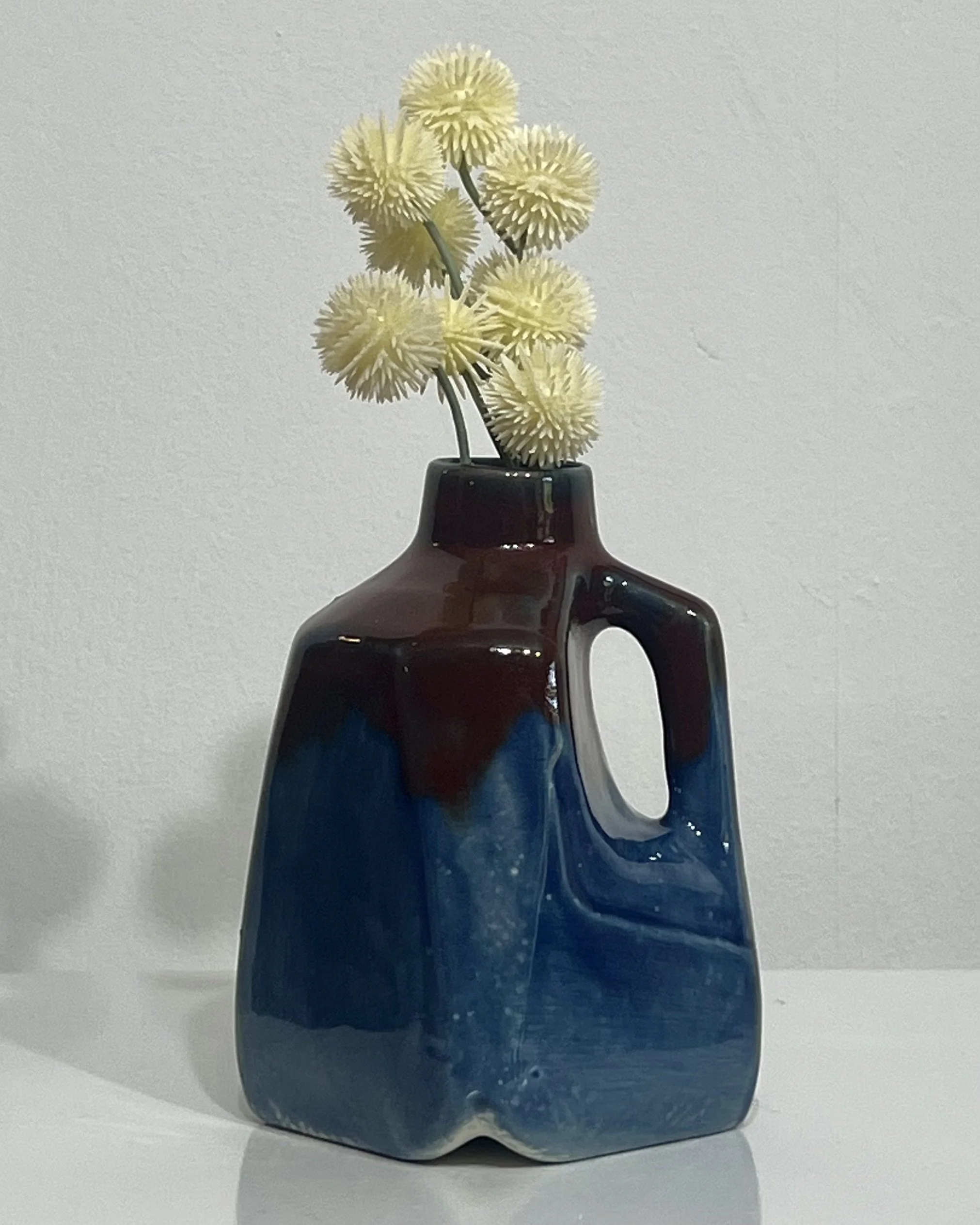 Handmade porcelain milk jug vase by Alissa Van Atta featuring Deep Sea and Deep Firebrick glazes in ocean blue and burgundy, displayed with pale flowers.
