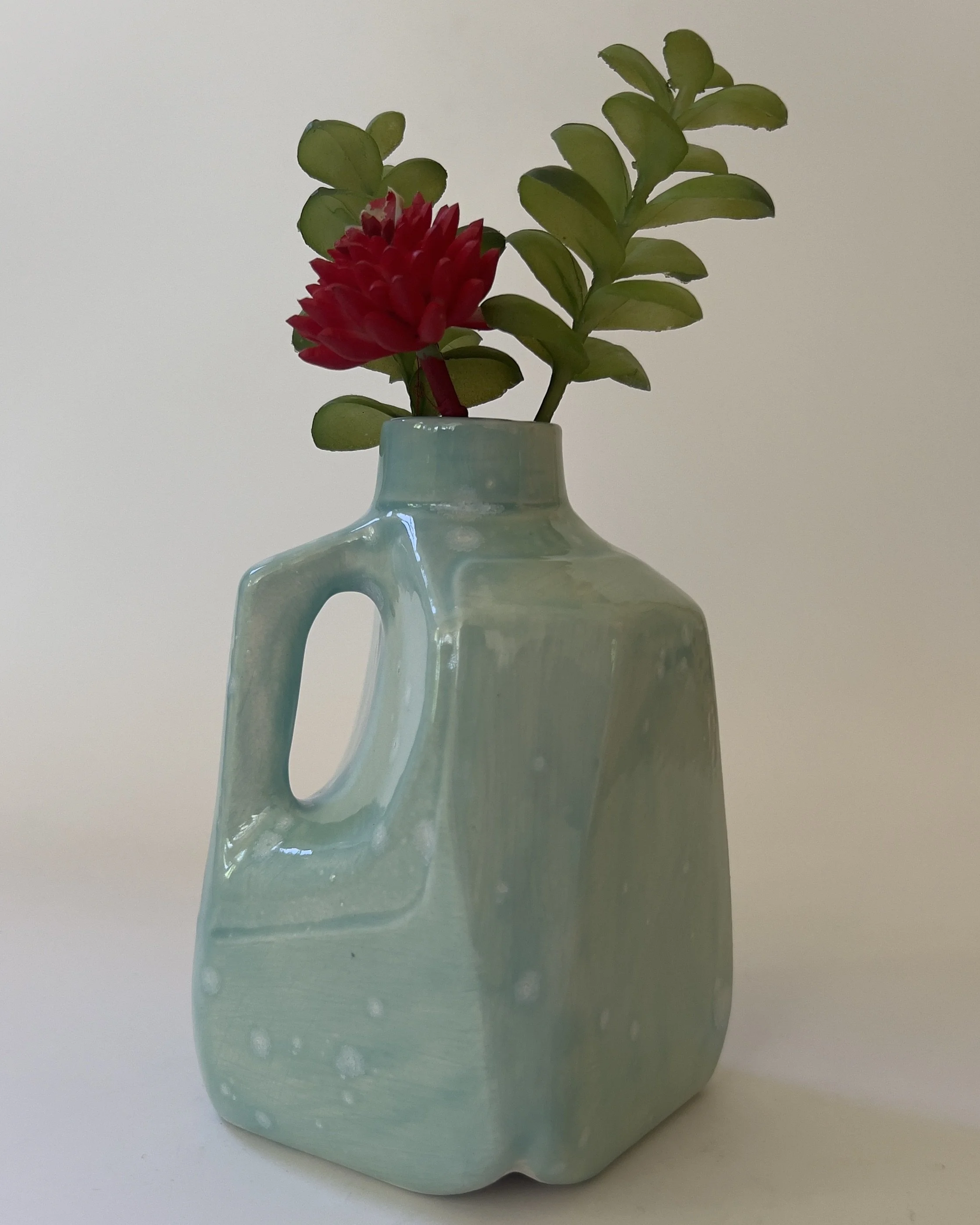 Small ceramic milk jug vase with celadon bloom glaze holding flowers
