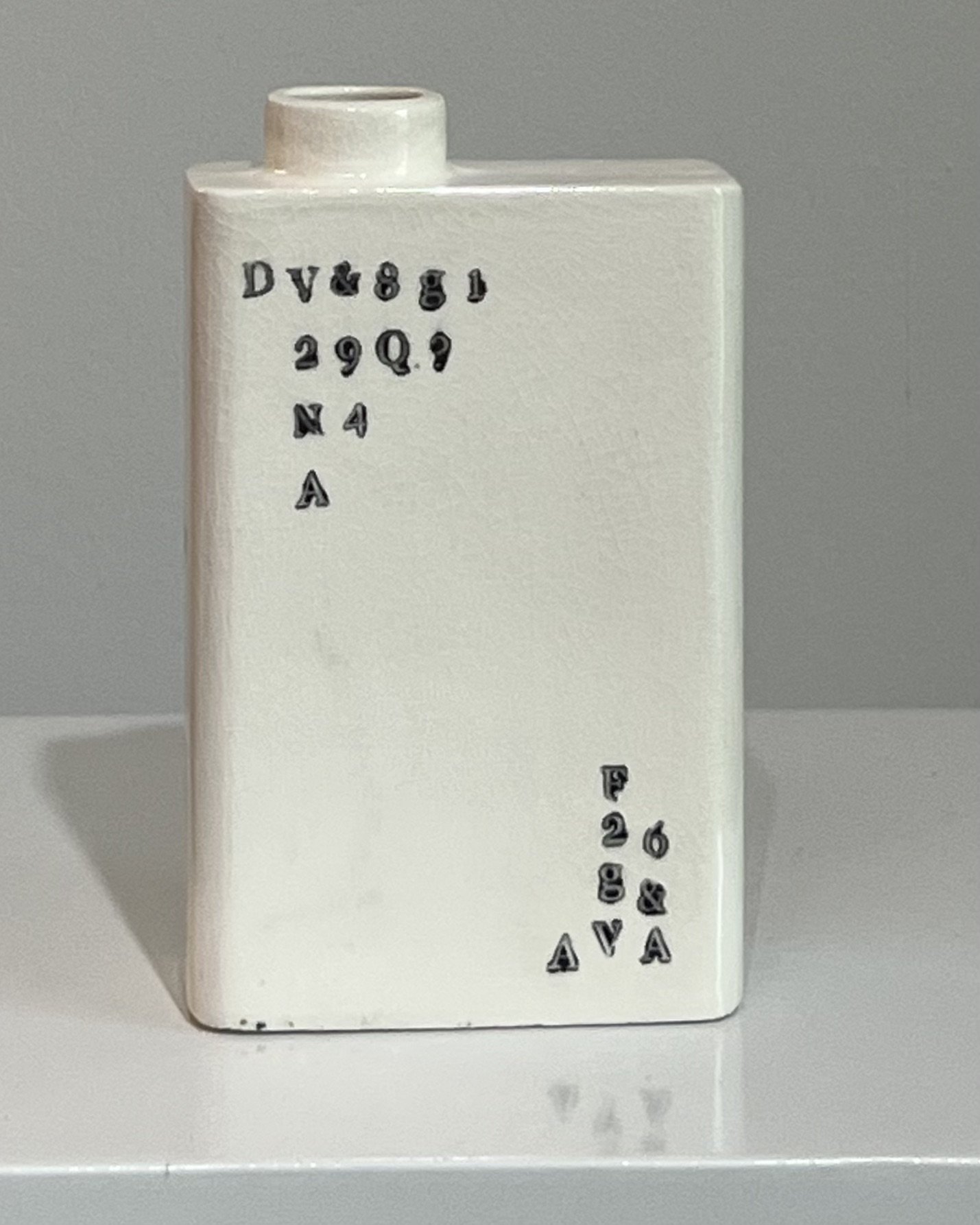 Front view of a handbuilt white porcelain milk carton with scattered black typographic impressions.