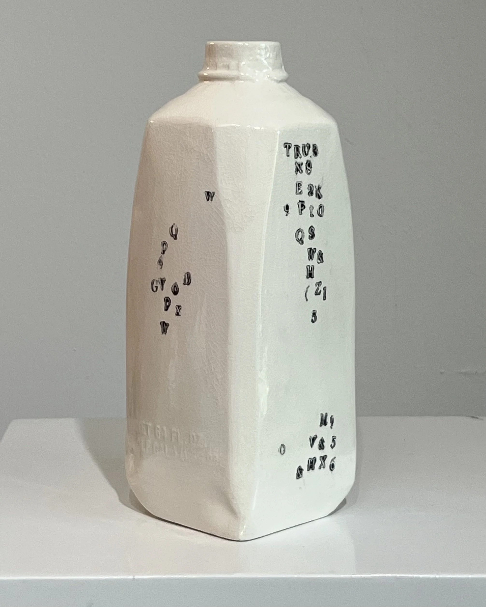 Angled left view of a contemporary tall porcelain milk jug featuring impressed black typography and glossy white glaze.