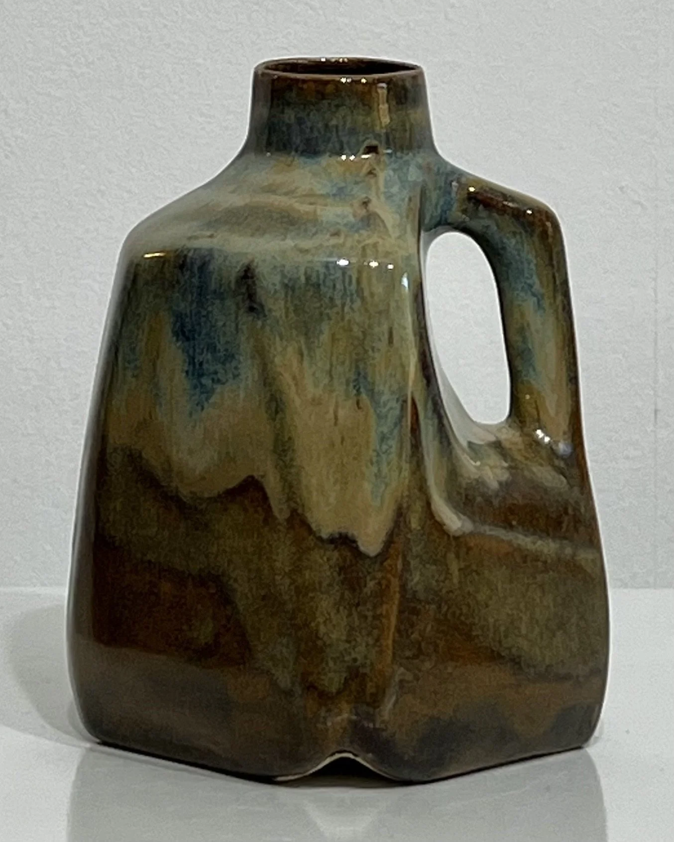 Front view of handmade porcelain milk jug with blue-green glaze flowing over rich earthy brown