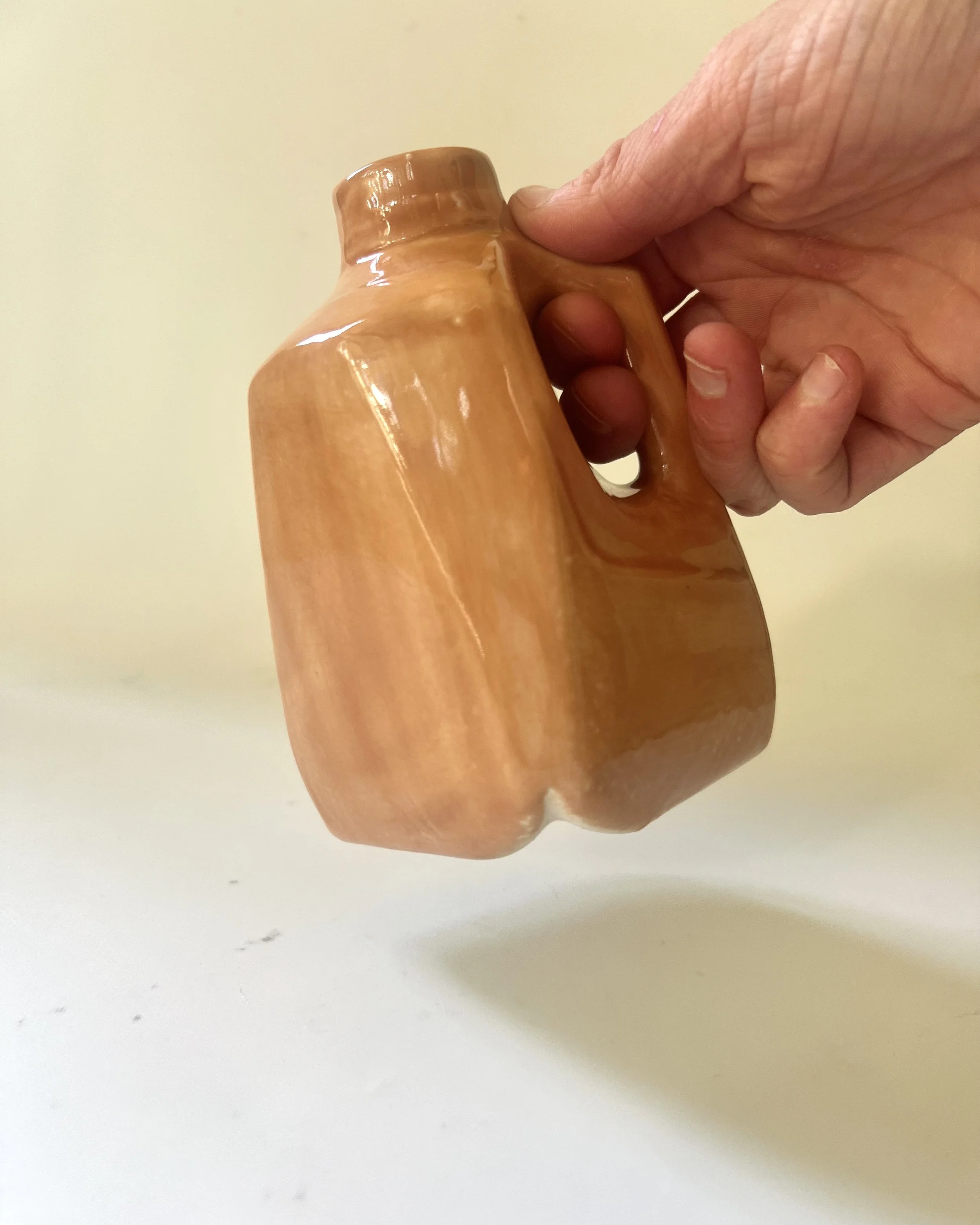 Porcelain milk jug vase suspended by its handle, showing the sculptural form and proportions.