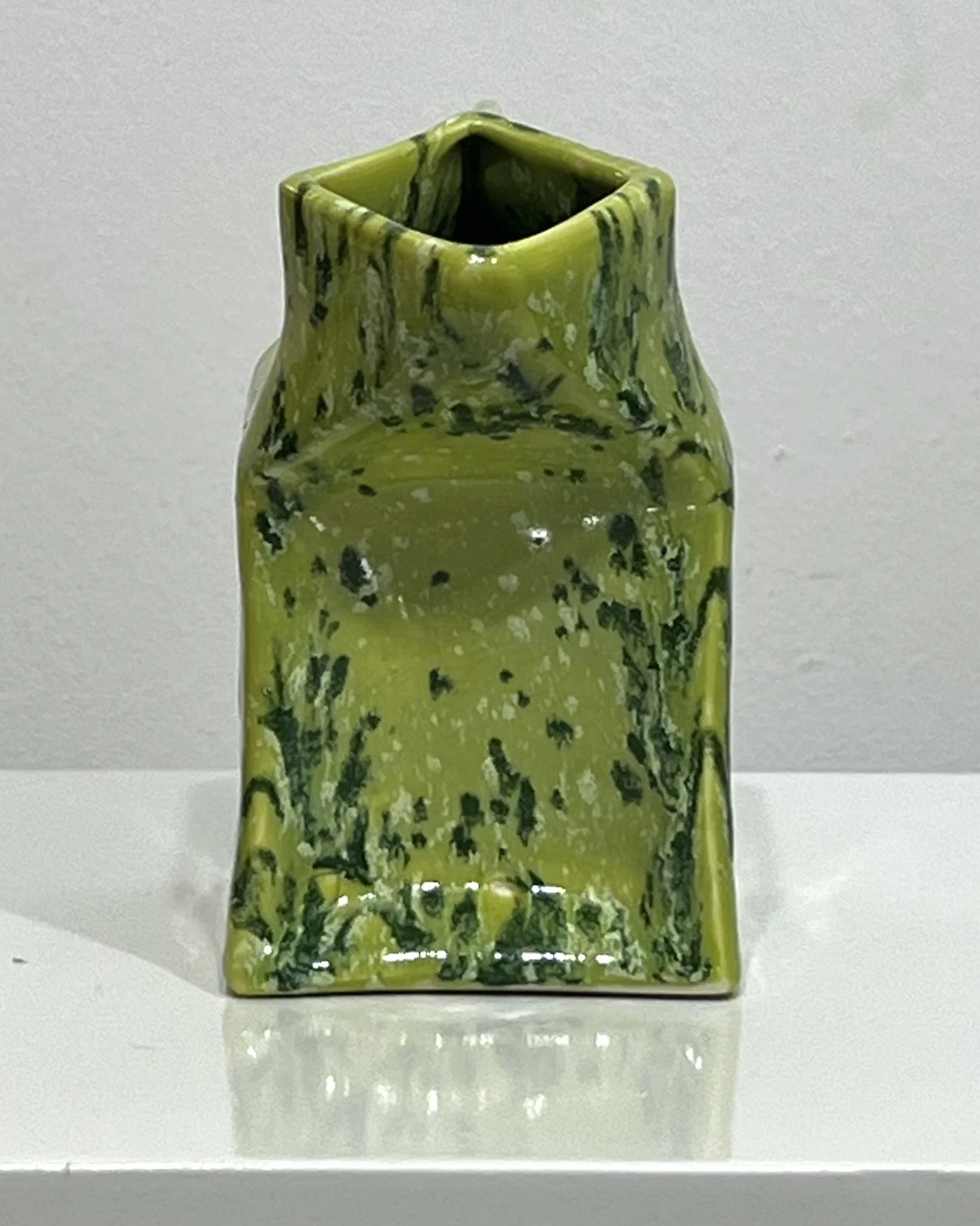 Handmade porcelain milk carton sculpture in Lime Shower glaze featuring chartreuse green and dark green speckled surface, shown as a contemporary ceramic art object.