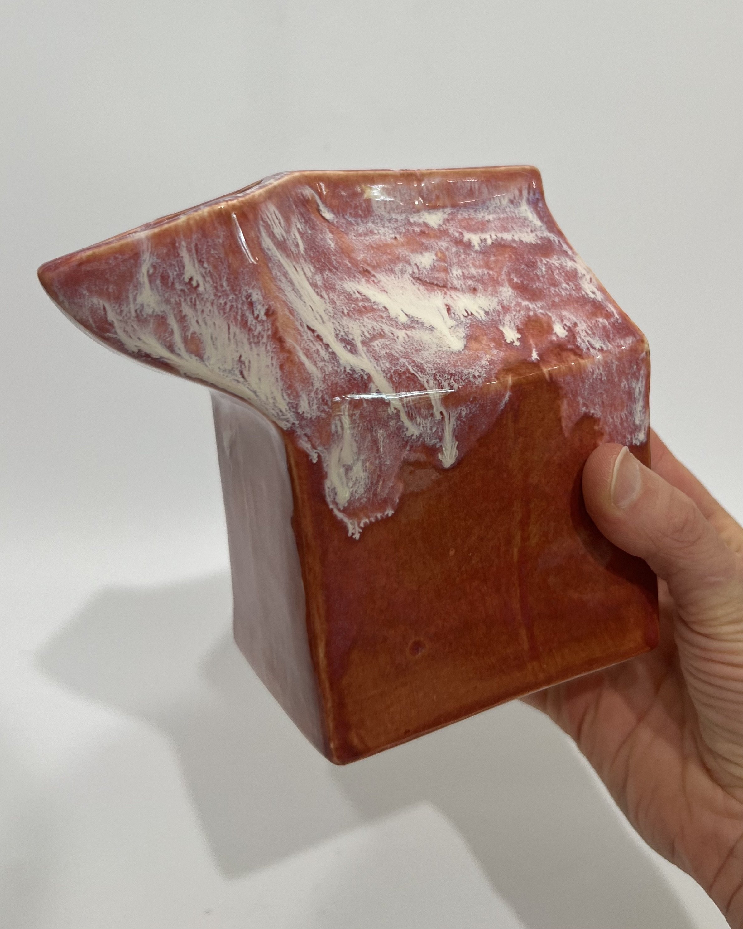 Hand holding the ceramic milk carton vase to show the scale and sculptural shape of the handmade vessel.