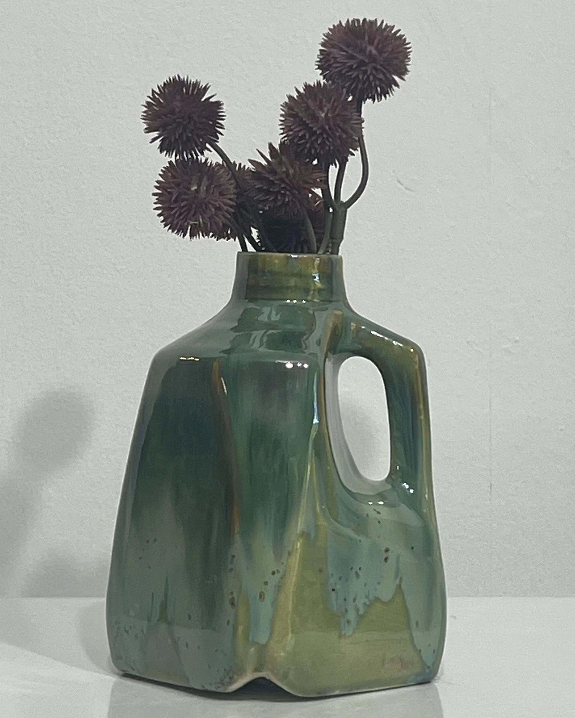 Handmade green porcelain milk jug vase with Micro Jade and Seaweed glazes, styled with decorative flowers.