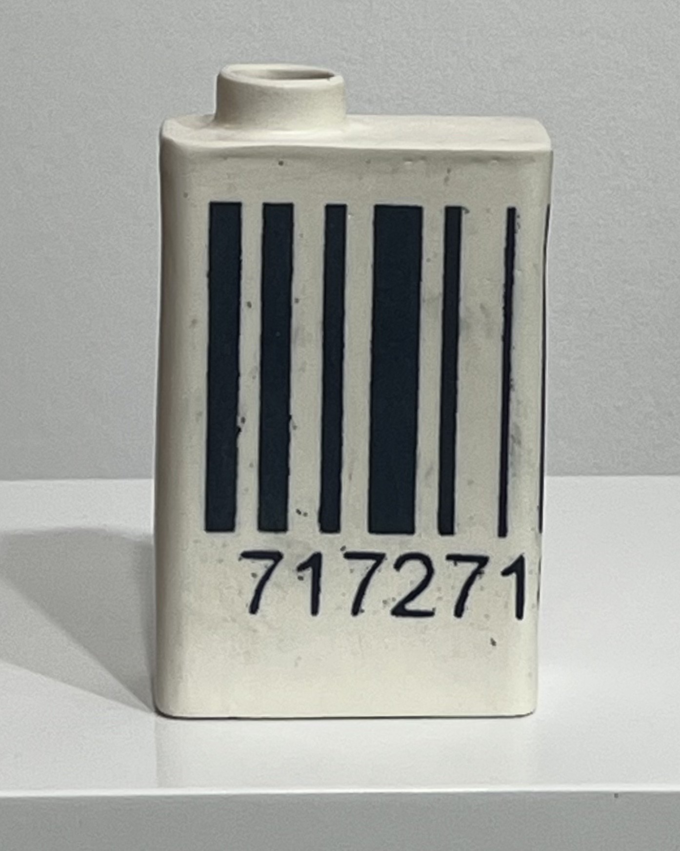 Front view of white porcelain milk carton with bold black barcode and hand-drawn numbers