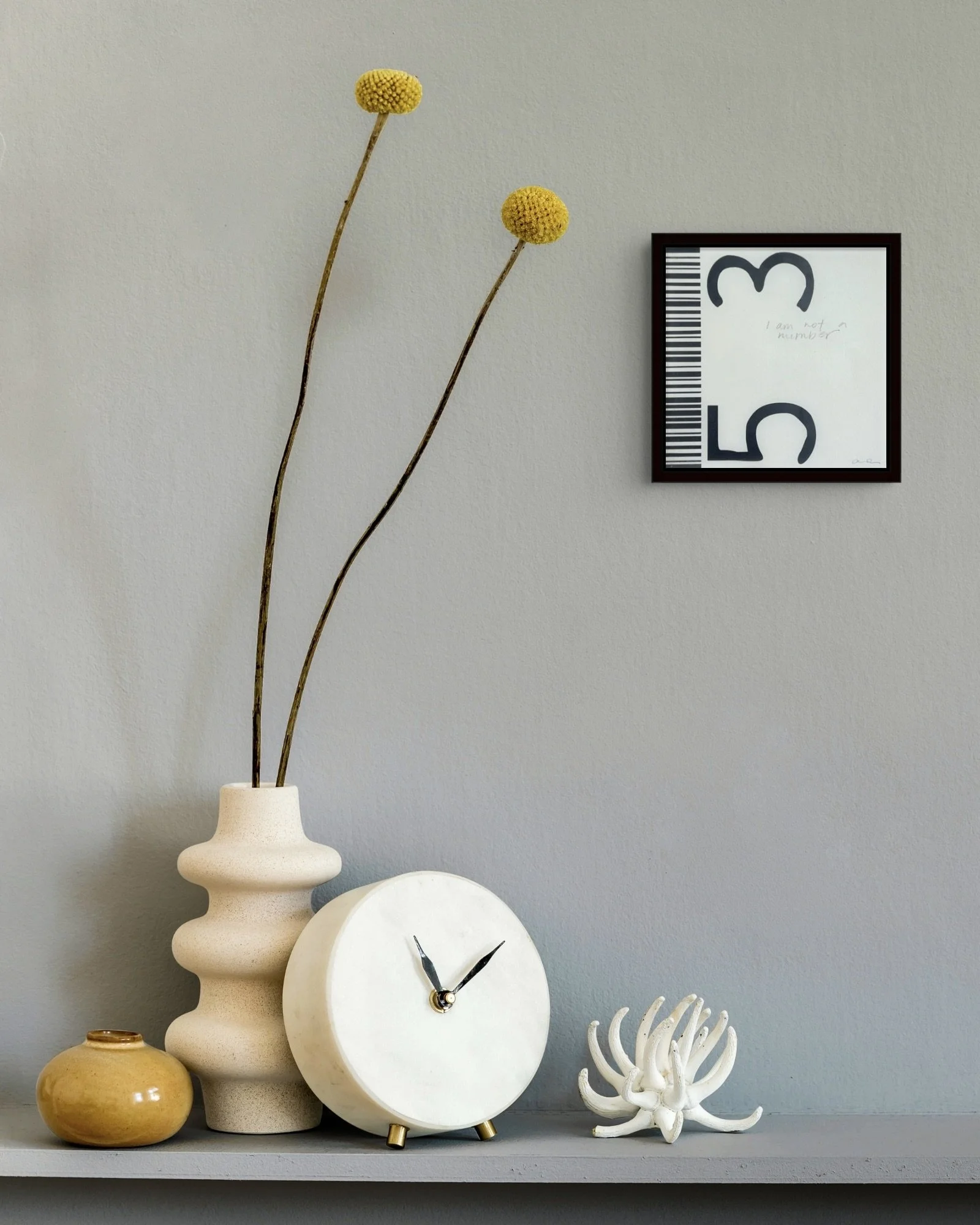 I Am Not a Number, a small framed contemporary feminist barcode artwork by Alissa Van Atta, displayed on a neutral wall above a decorative console with a vase and clock.