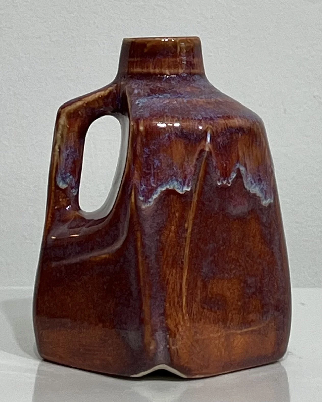 Back view of burgundy porcelain milk jug with integrated handle and flowing glaze