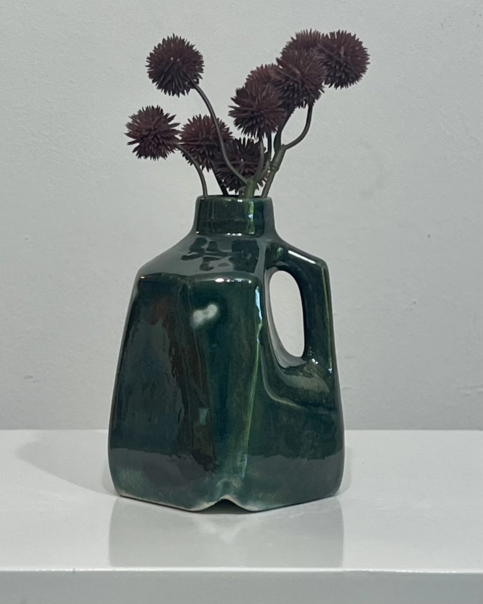 Handmade porcelain milk jug vase glazed in Vintage Gold over Rainforest with deep green and bronze tones, displayed with dried flowers.