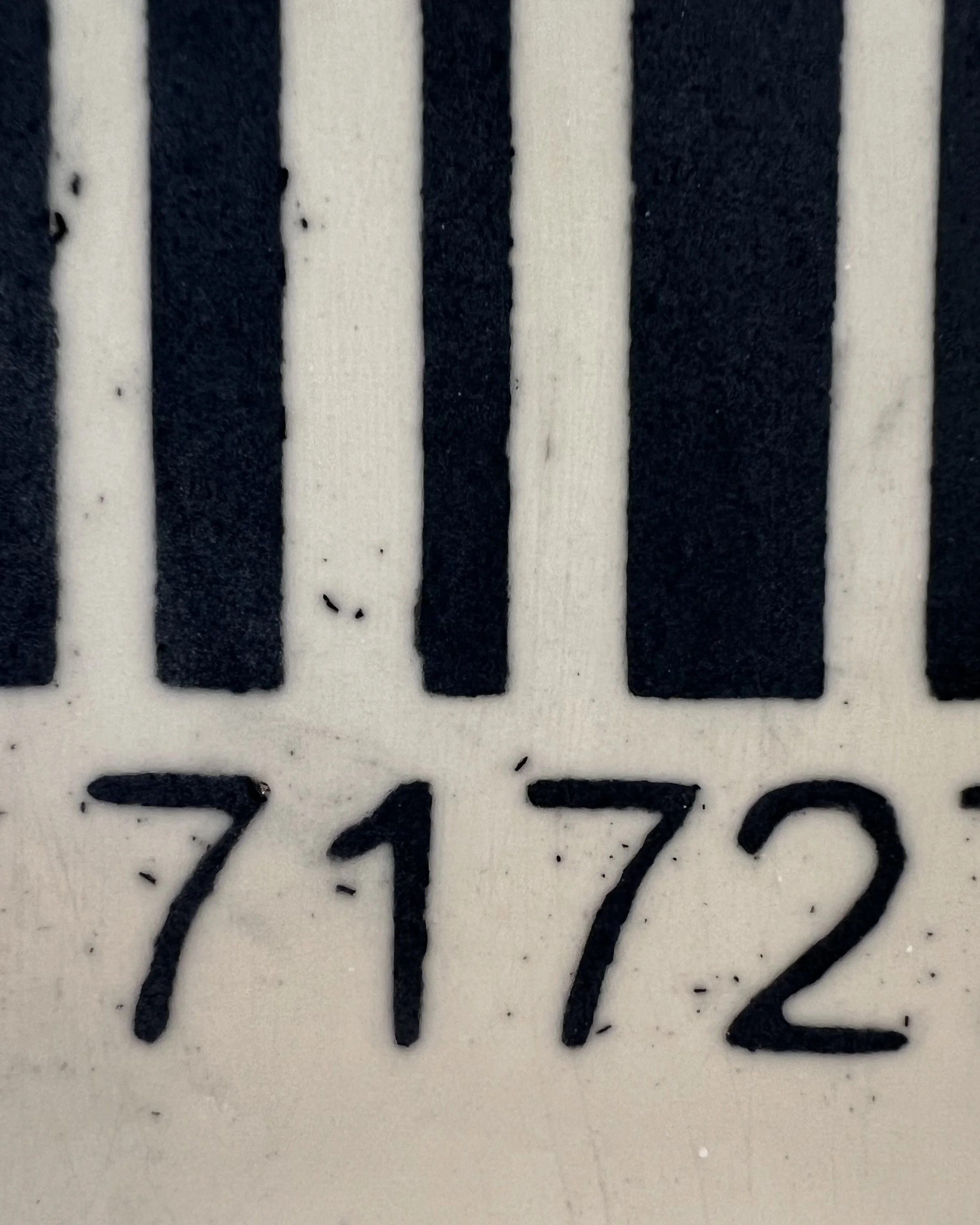 Close-up detail of black barcode lines and hand-drawn numbers on white porcelain