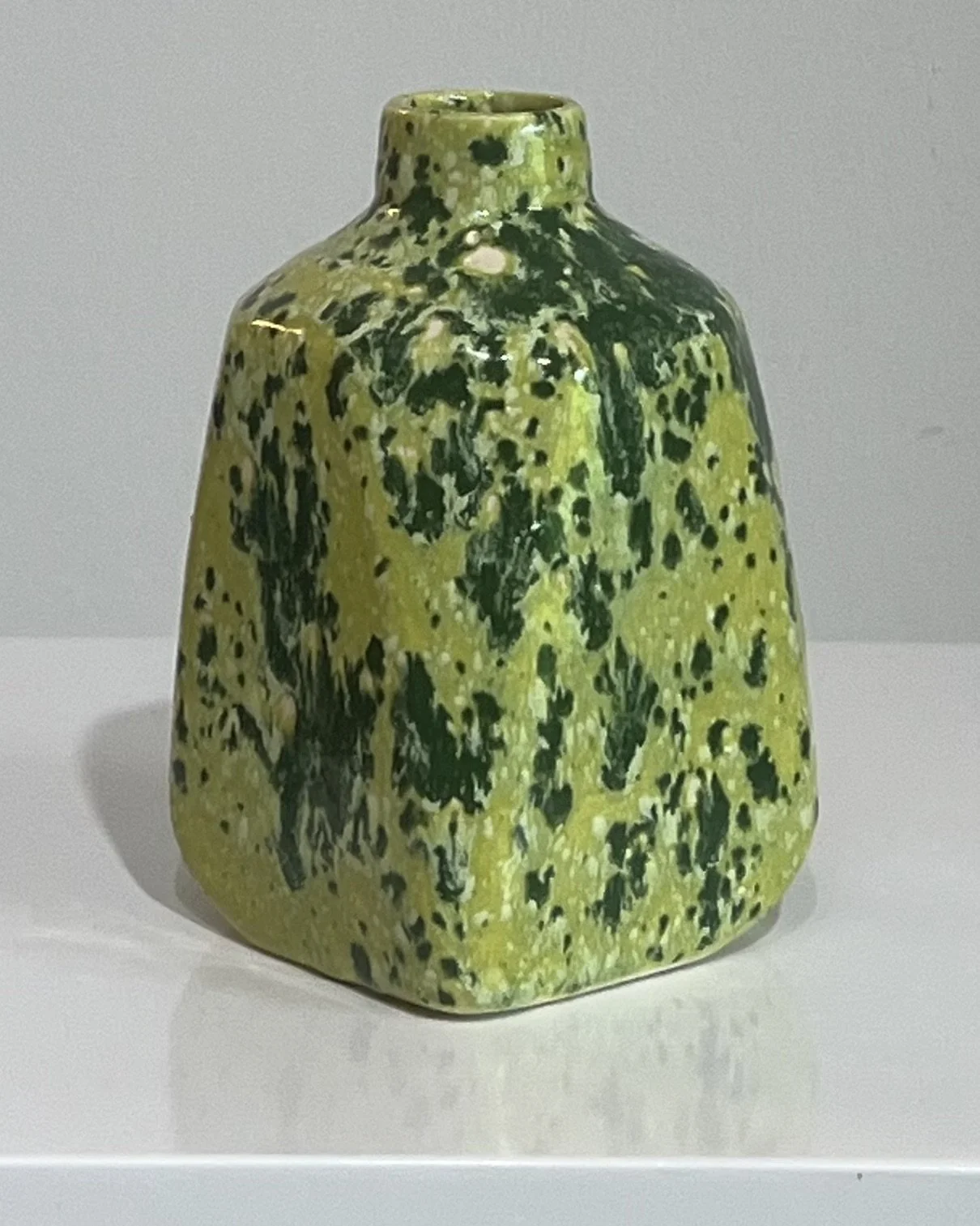 Back view of a handmade porcelain milk jug with a layered green speckled glaze.