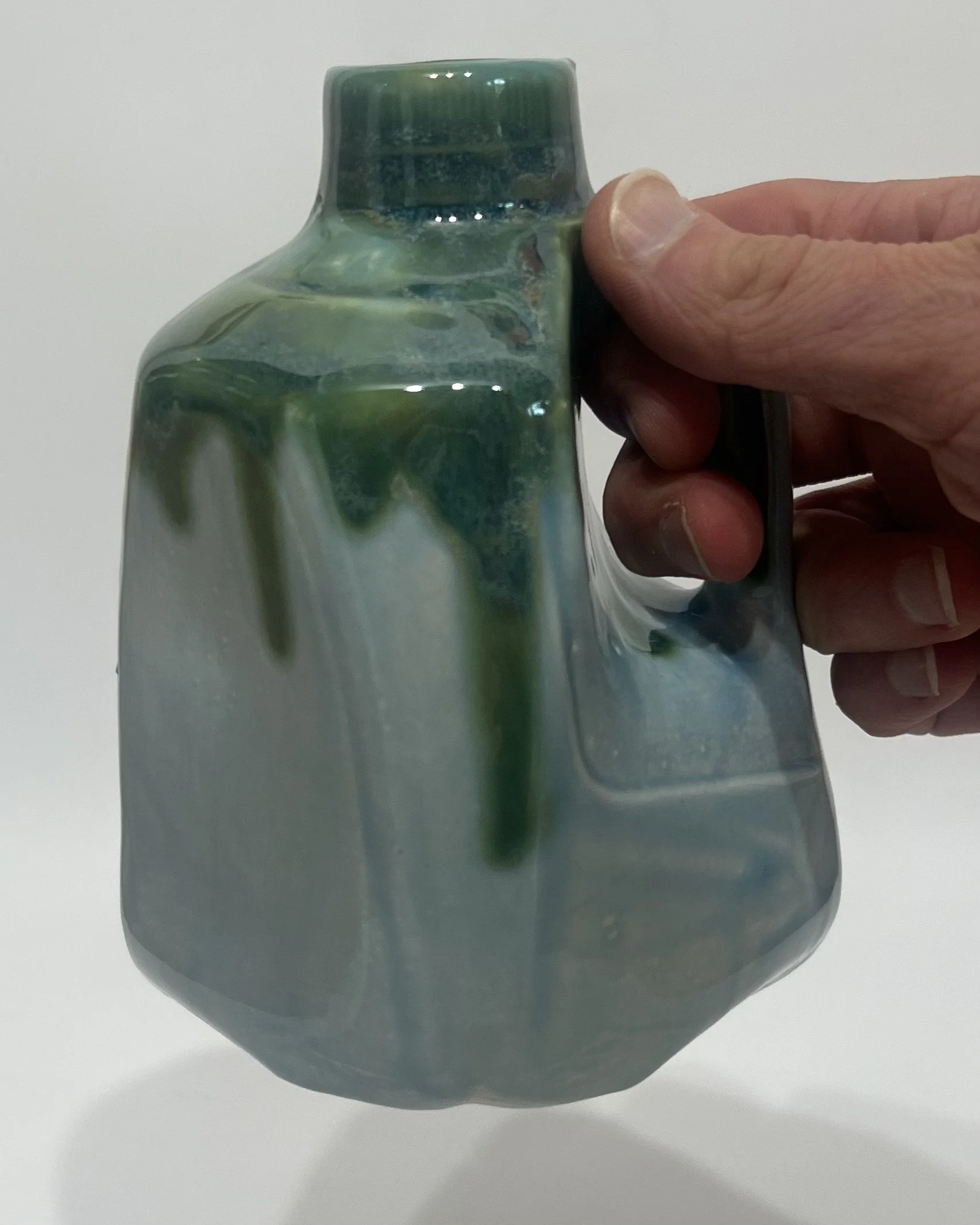 Hand holding the handle of a small ceramic milk jug sculpture to show the scale and handmade form.