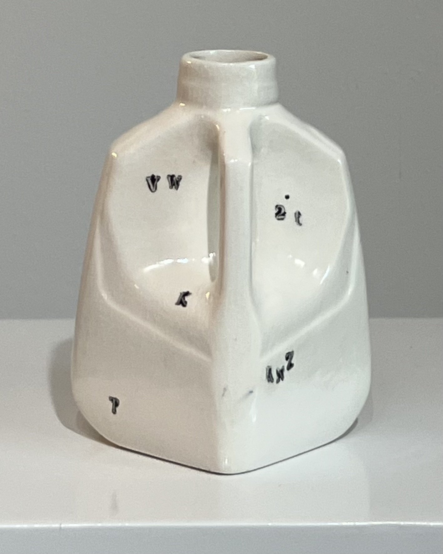 Angled right view of a white porcelain milk jug featuring fragmented black typography and handbuilt construction.