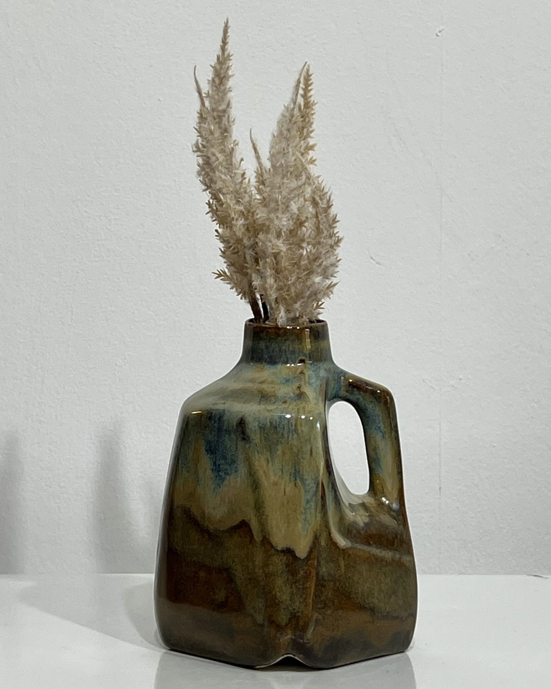 Handmade porcelain milk jug vase 26.124 by Alissa Van Atta, featuring smoky blue Blue Rutile glaze flowing over warm brown Iron Lustre glaze, styled with dried botanical stems.