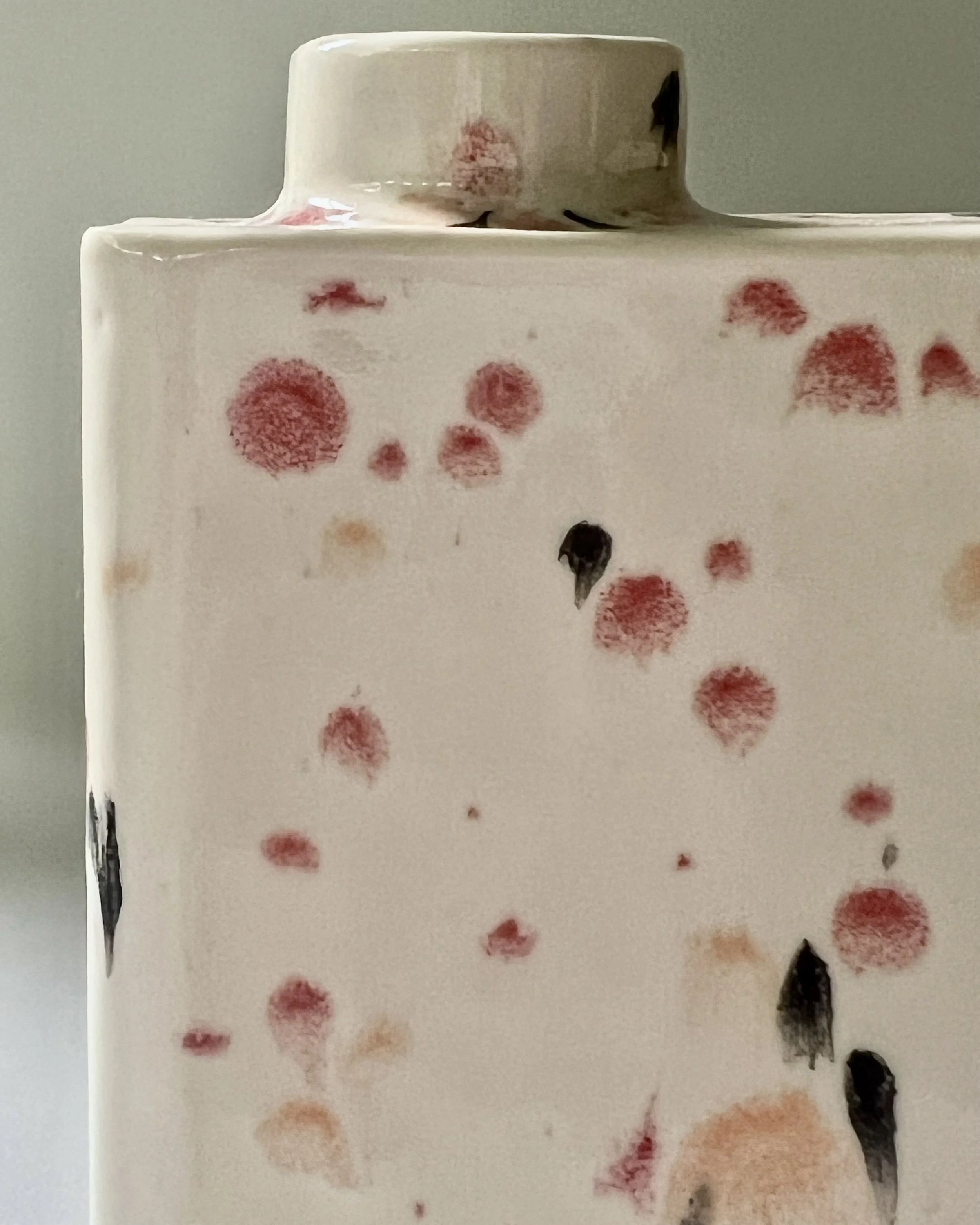 Close-up detail of Poppy Fields porcelain carton vase C26.6 highlighting red and peach speckles with black accents on cream glaze.