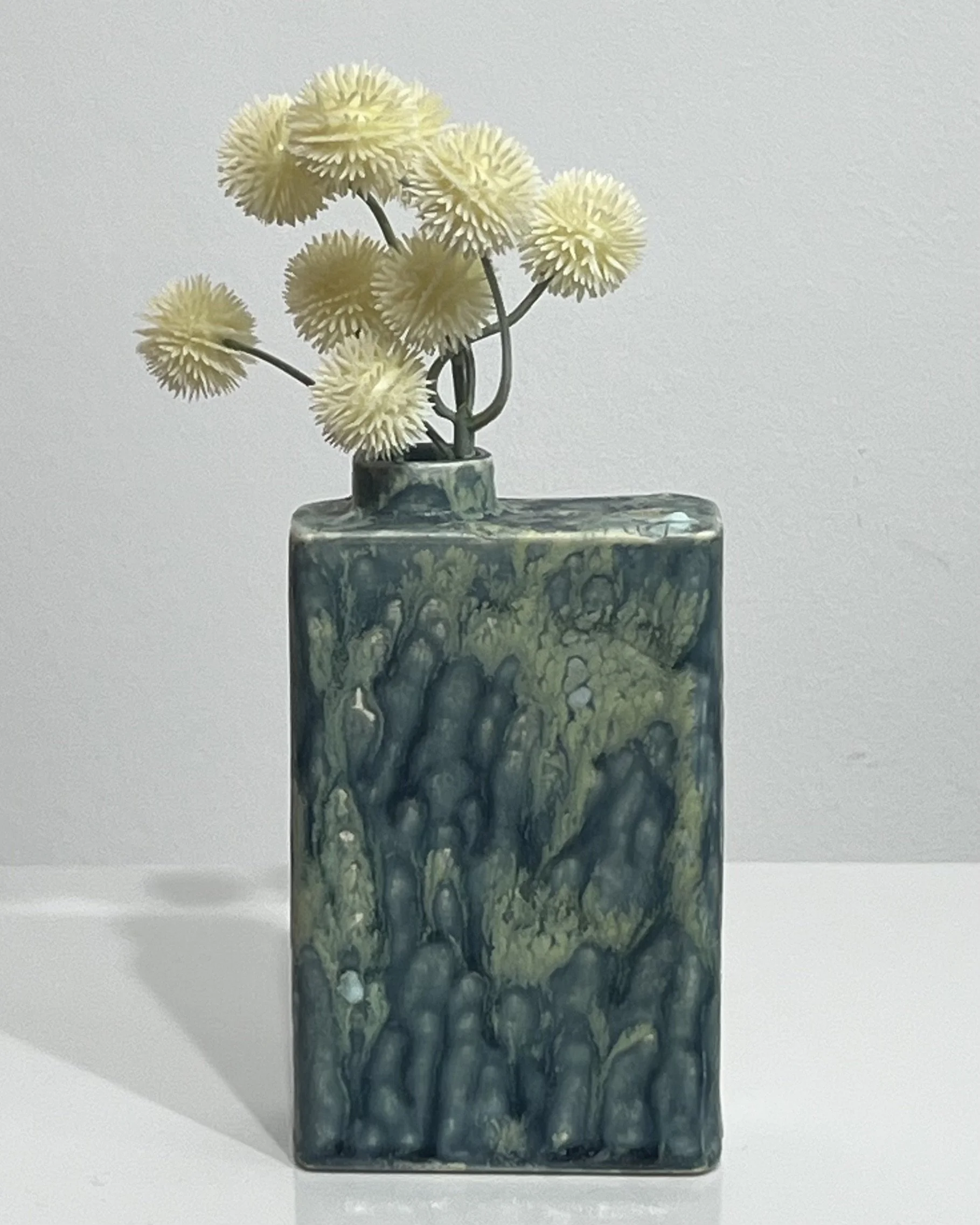 Handmade blue-green porcelain Carton vessel by Alissa Van Atta displayed with flowers.