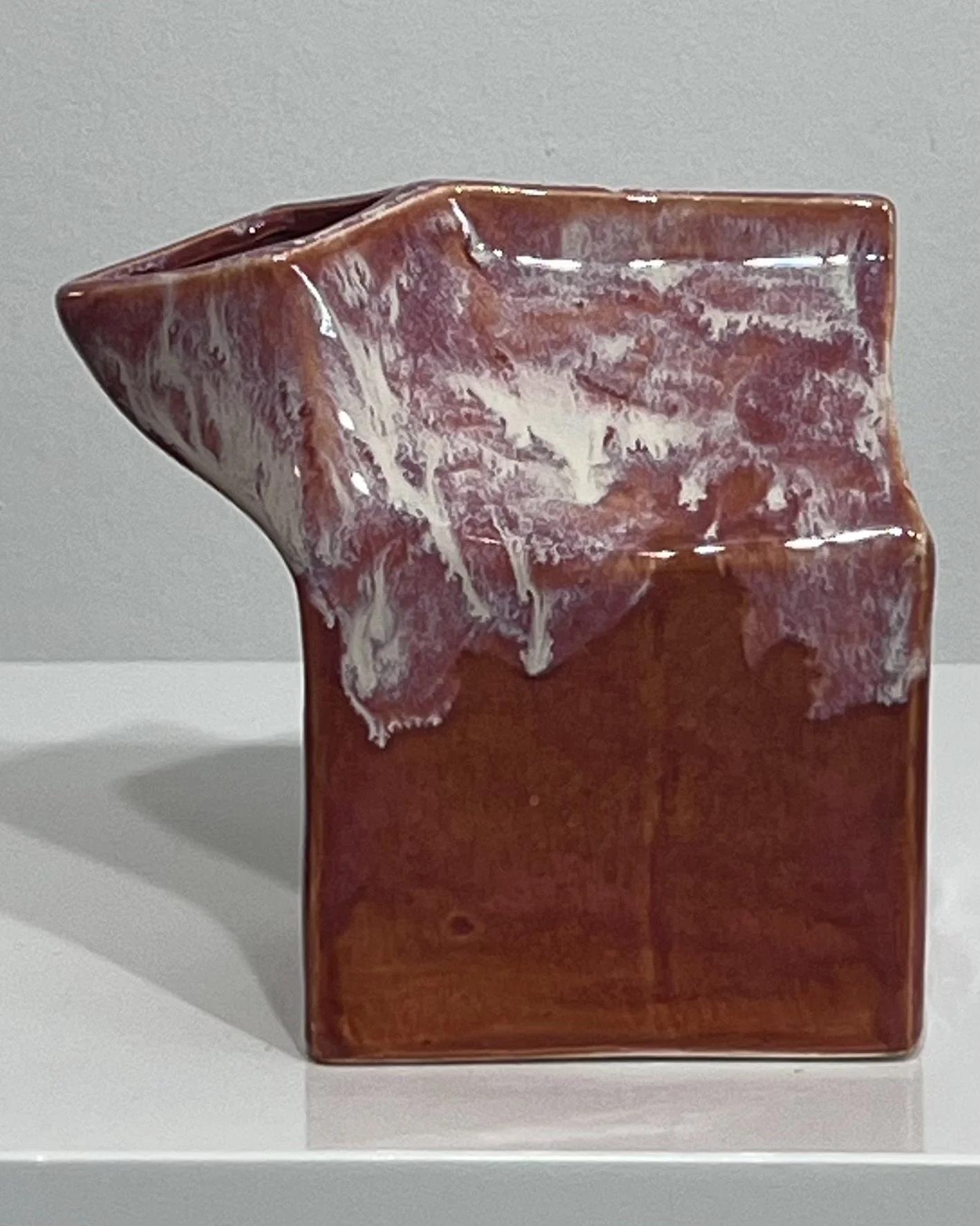 Front angled view of a handbuilt ceramic milk carton with rust red, cream, and plum glaze.