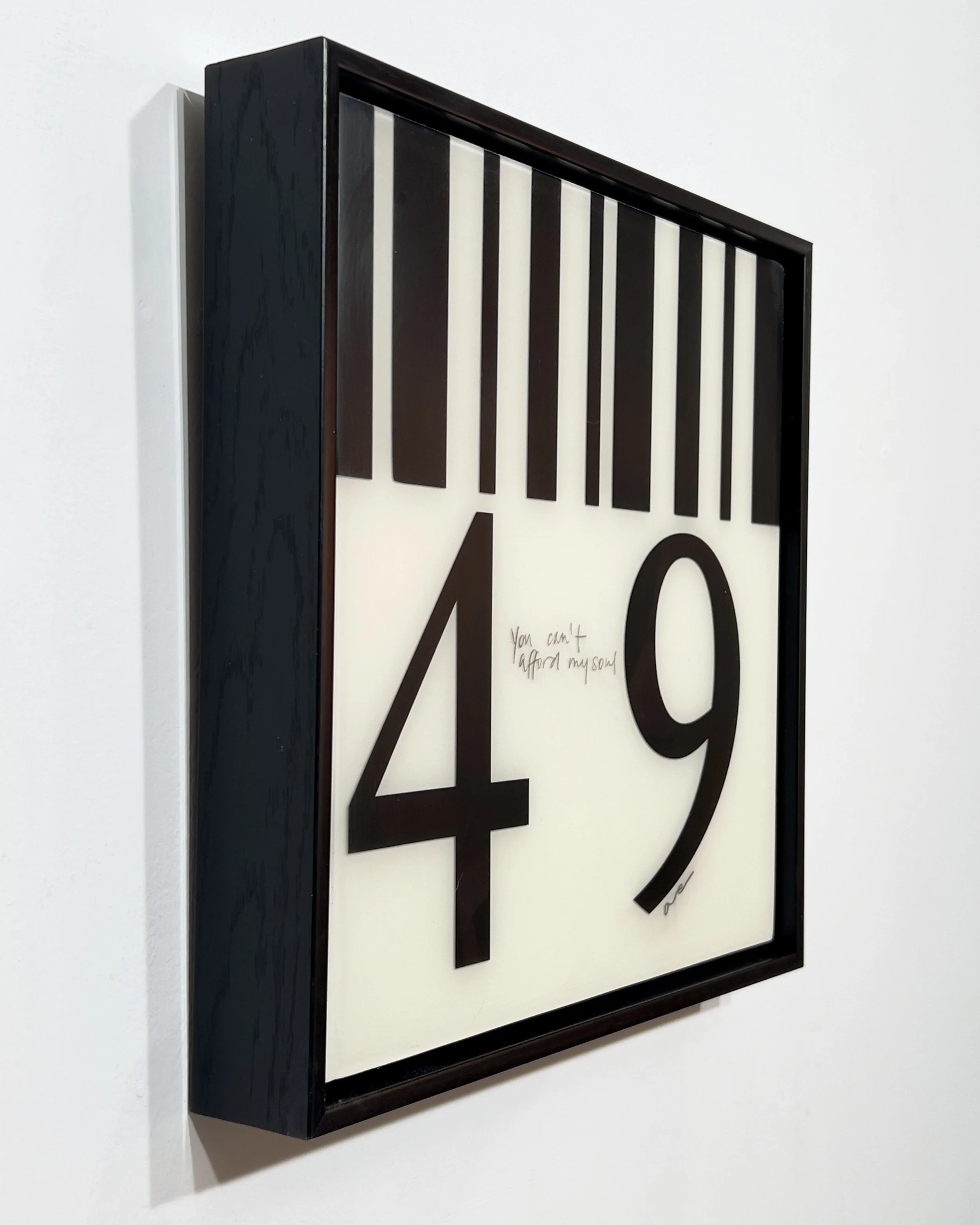 Angled view of You Can't Afford My Soul by Alissa Van Atta, a 12 by 12 inch black-and-white resin and acrylic barcode collage on wood, photographed in a black frame.