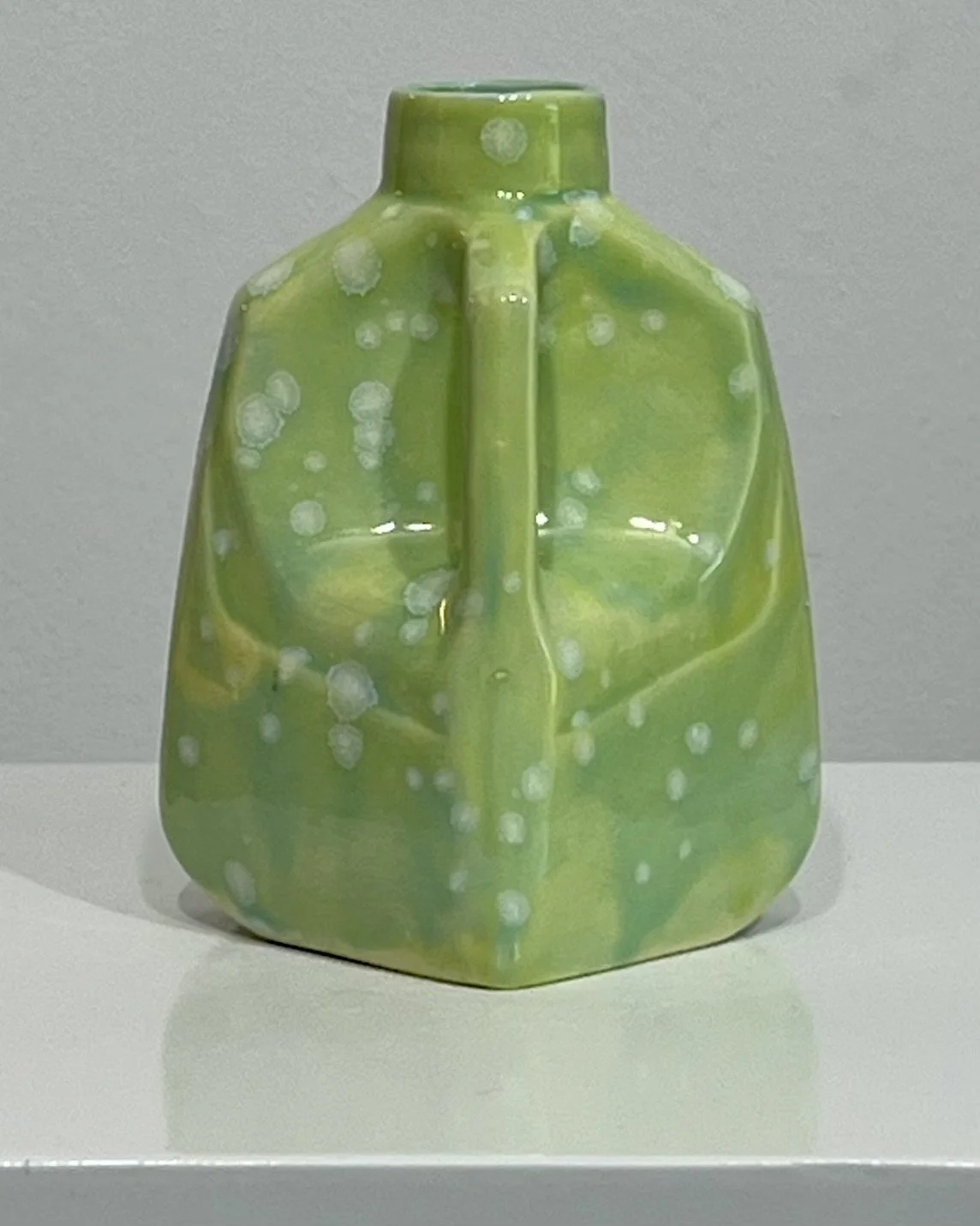 Back view of handmade porcelain milk jug with flowing green glaze and crystalline bloom pattern.