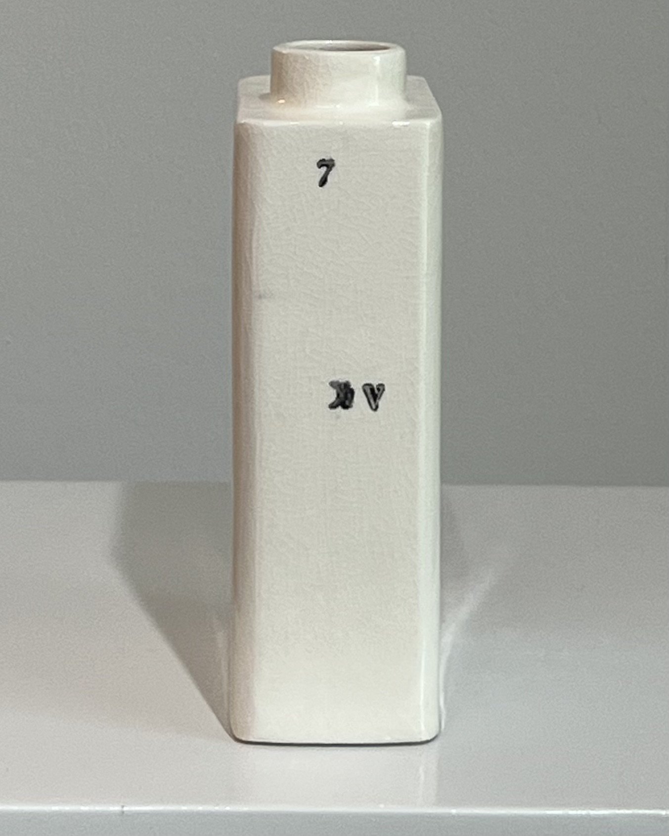 Side view of a handbuilt porcelain milk carton highlighting its sculptural form and typographic surface.