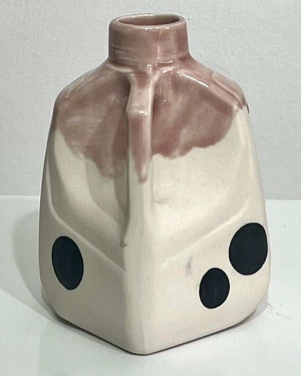Angled view of porcelain milk jug No. 26.149 with its handle on the right, showing oversized black polka dots and dusty-rose glaze flowing over the shoulders.