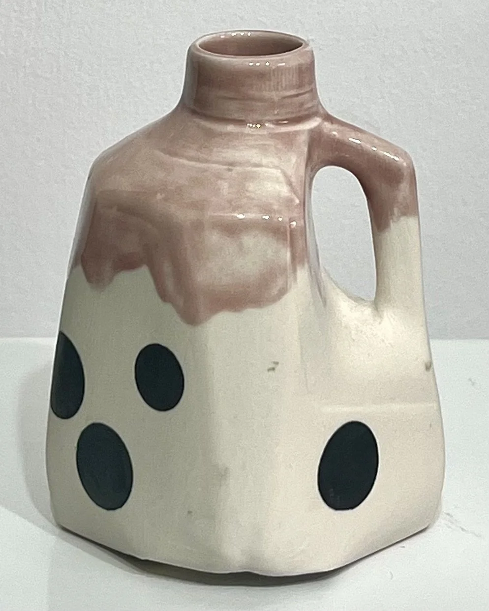 Front view of handmade porcelain milk jug No. 26.149 by Alissa Van Atta, featuring large black polka dots on a creamy white body and soft rose-mauve Weeping Plum glaze.
