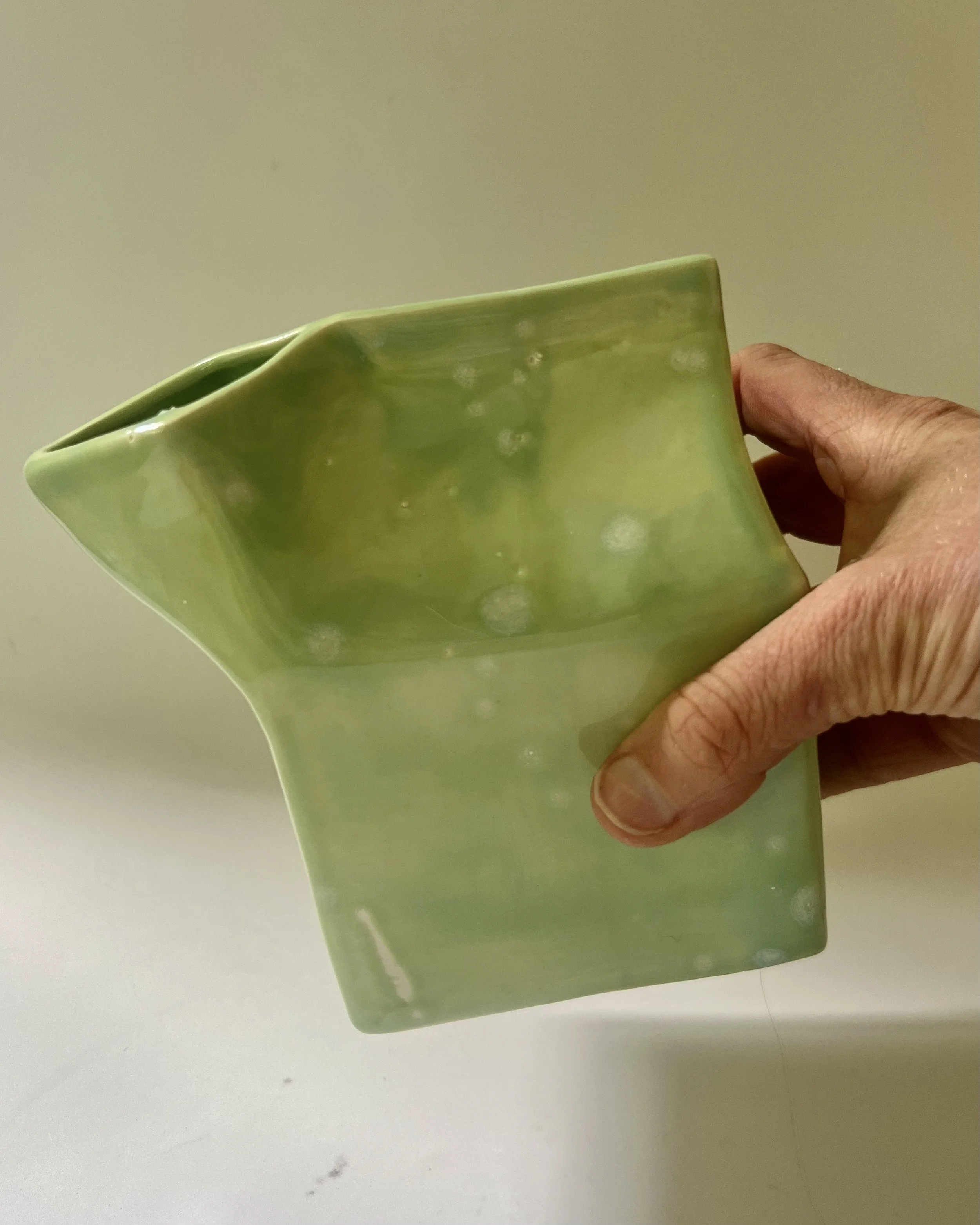 Hand holding porcelain milk carton to show scale and handcrafted form.