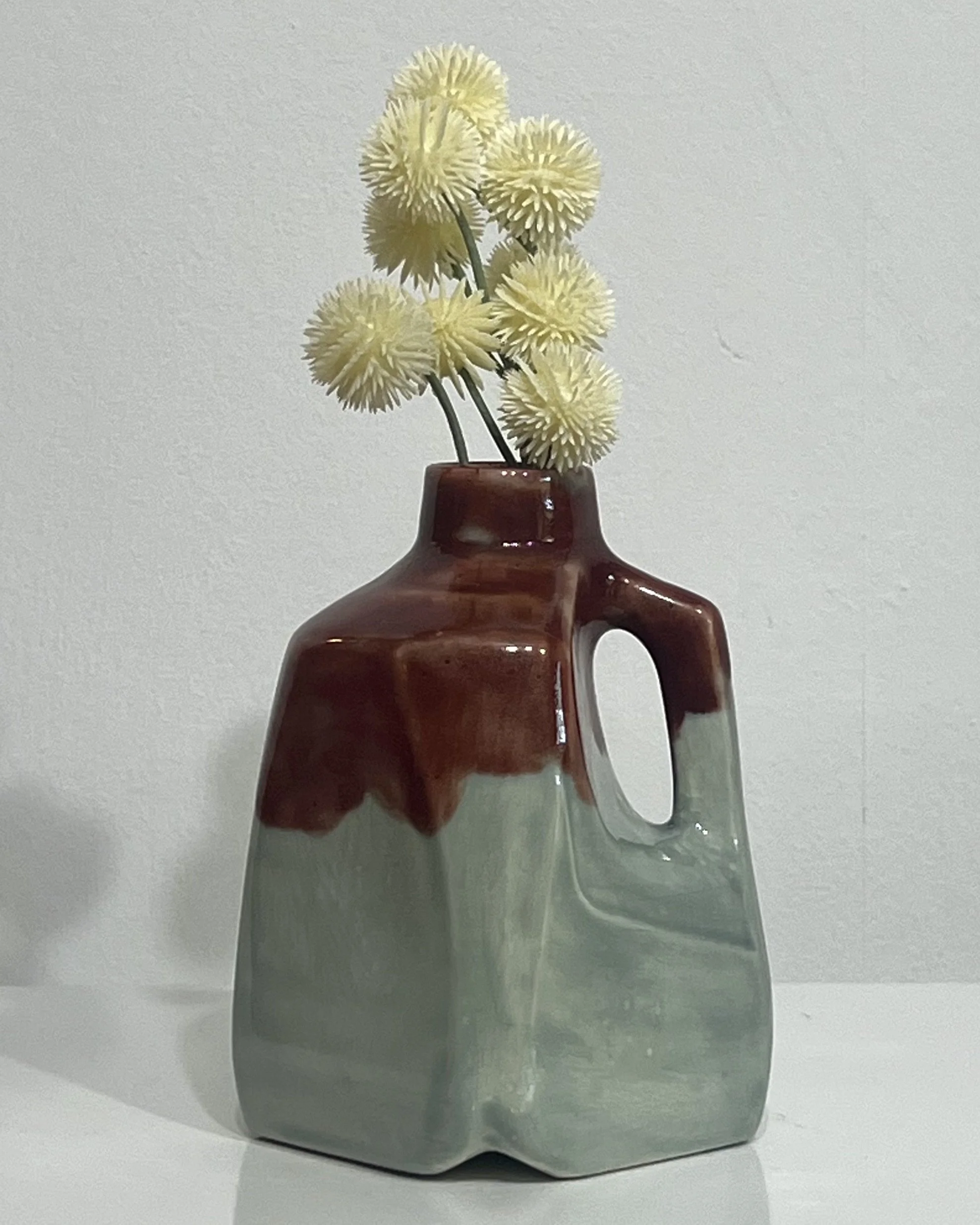 Handmade porcelain milk jug vase by Alissa Van Atta featuring Fog and Deep Firebrick glazes in rich burgundy-red and muted sage-green tones, displayed with small flowers.
