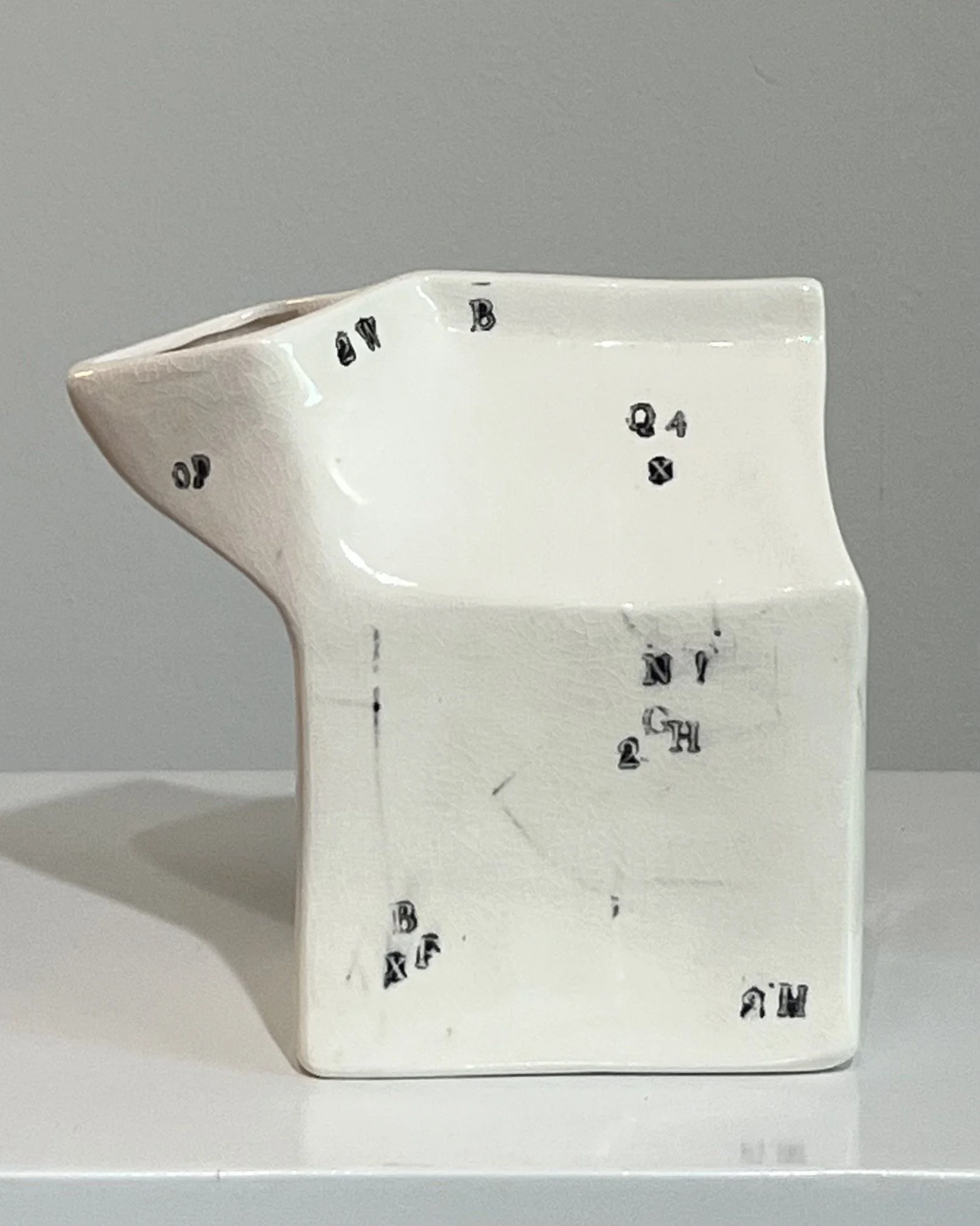 Rear view of a handbuilt porcelain milk carton with glossy white glaze and scattered black typography.