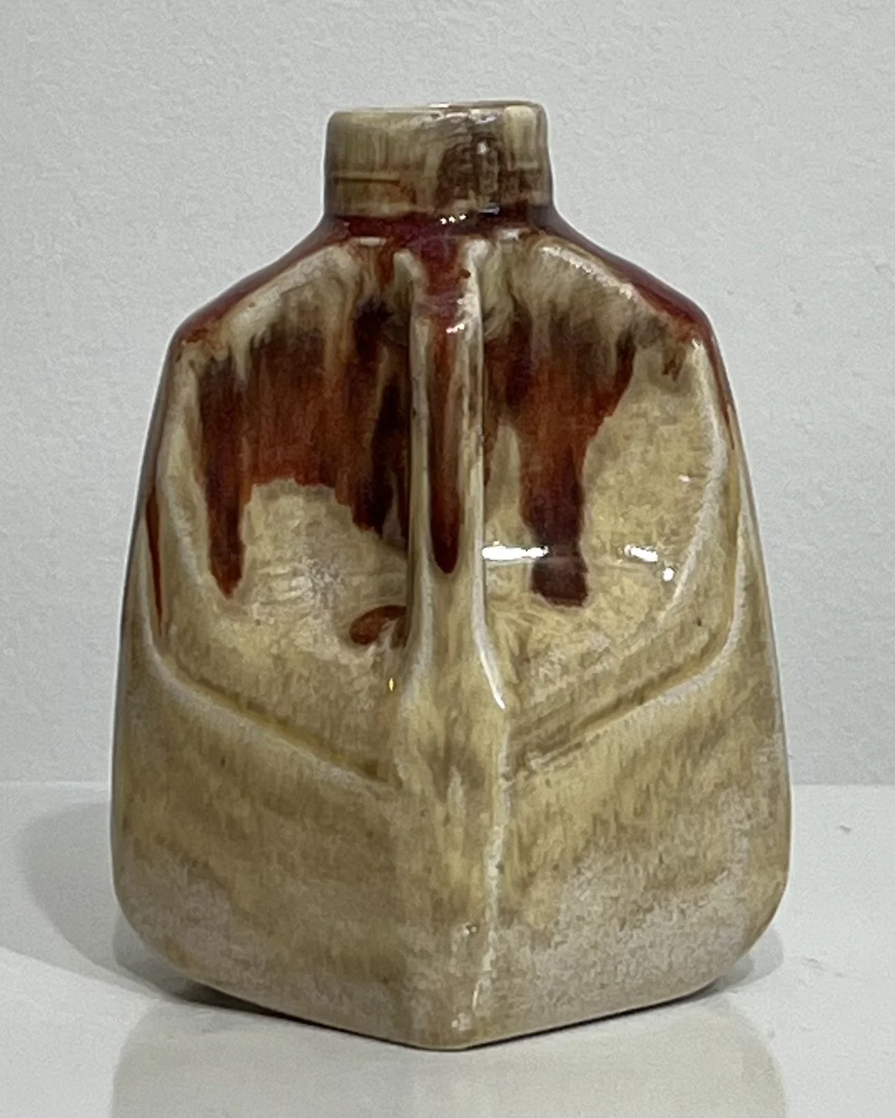 Angled view of handmade porcelain milk jug showing sculptural form and flowing reddish glaze