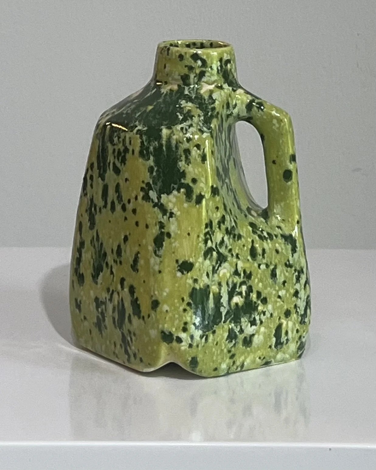 Front angled view of a handmade porcelain milk jug featuring a vibrant green speckled glaze.