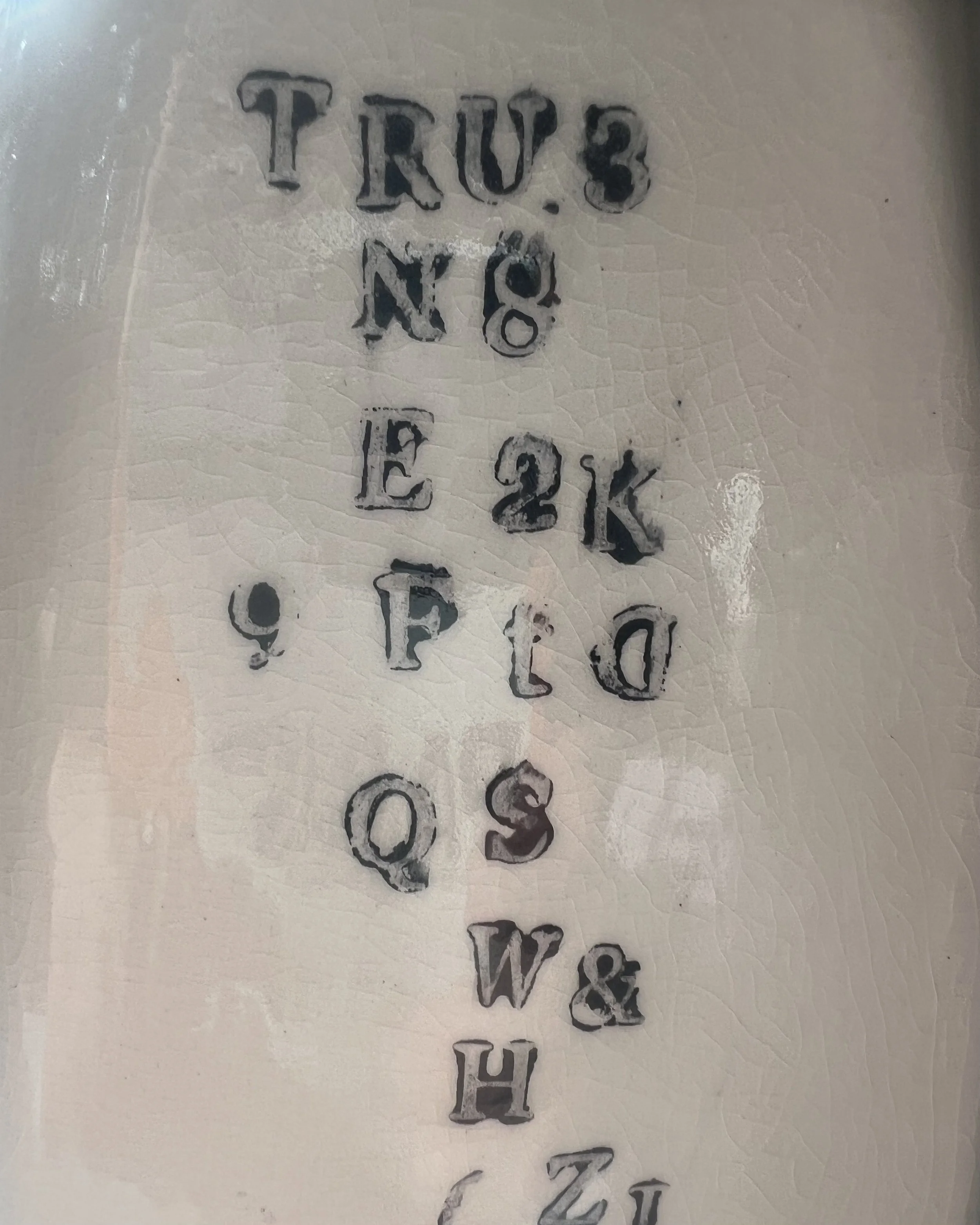 Close-up of impressed black typography on the surface of a handbuilt tall porcelain milk jug.