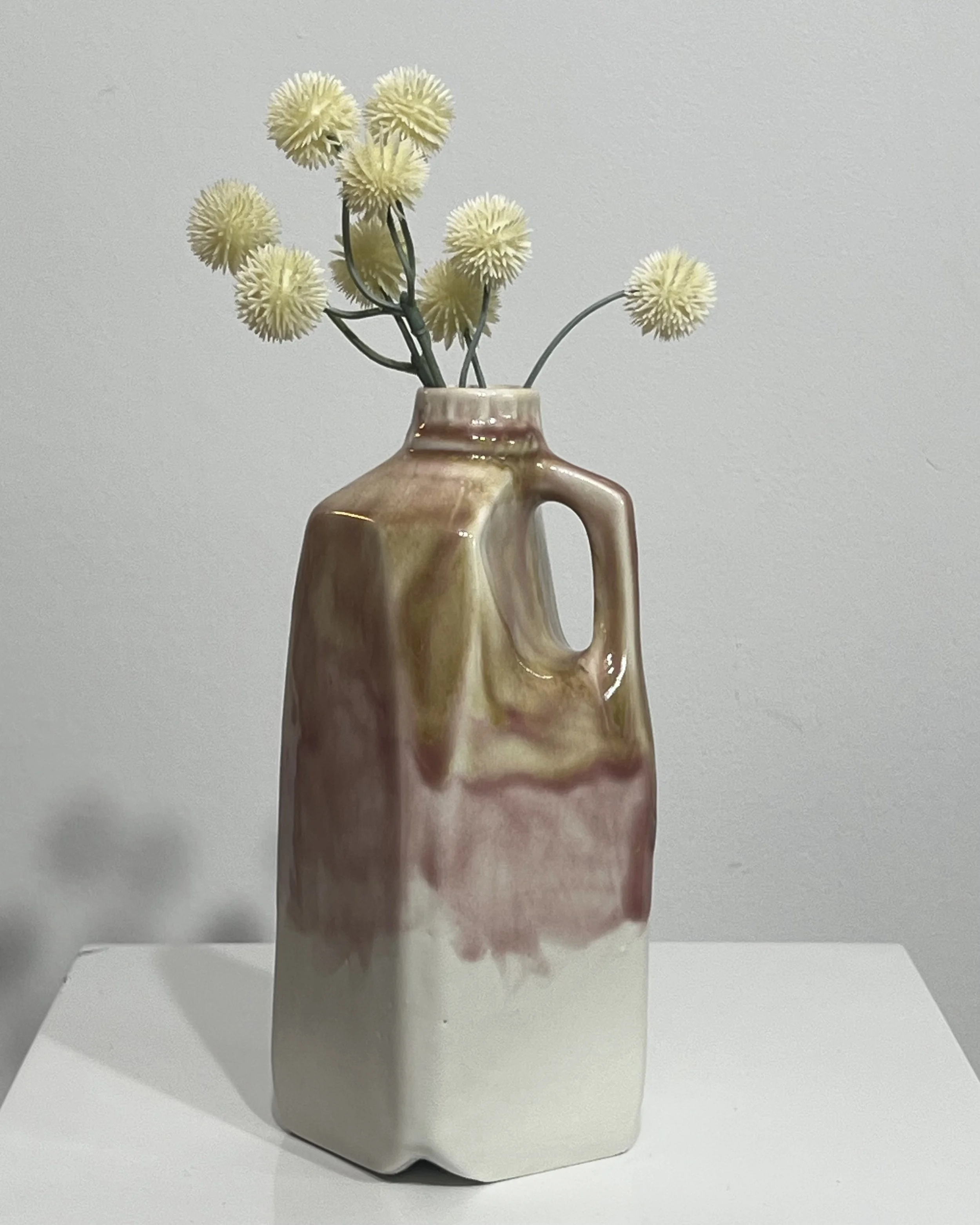 Tall handmade ceramic milk jug vase with cream flowers, layered in olive green, soft pink, plum, and white glazes.