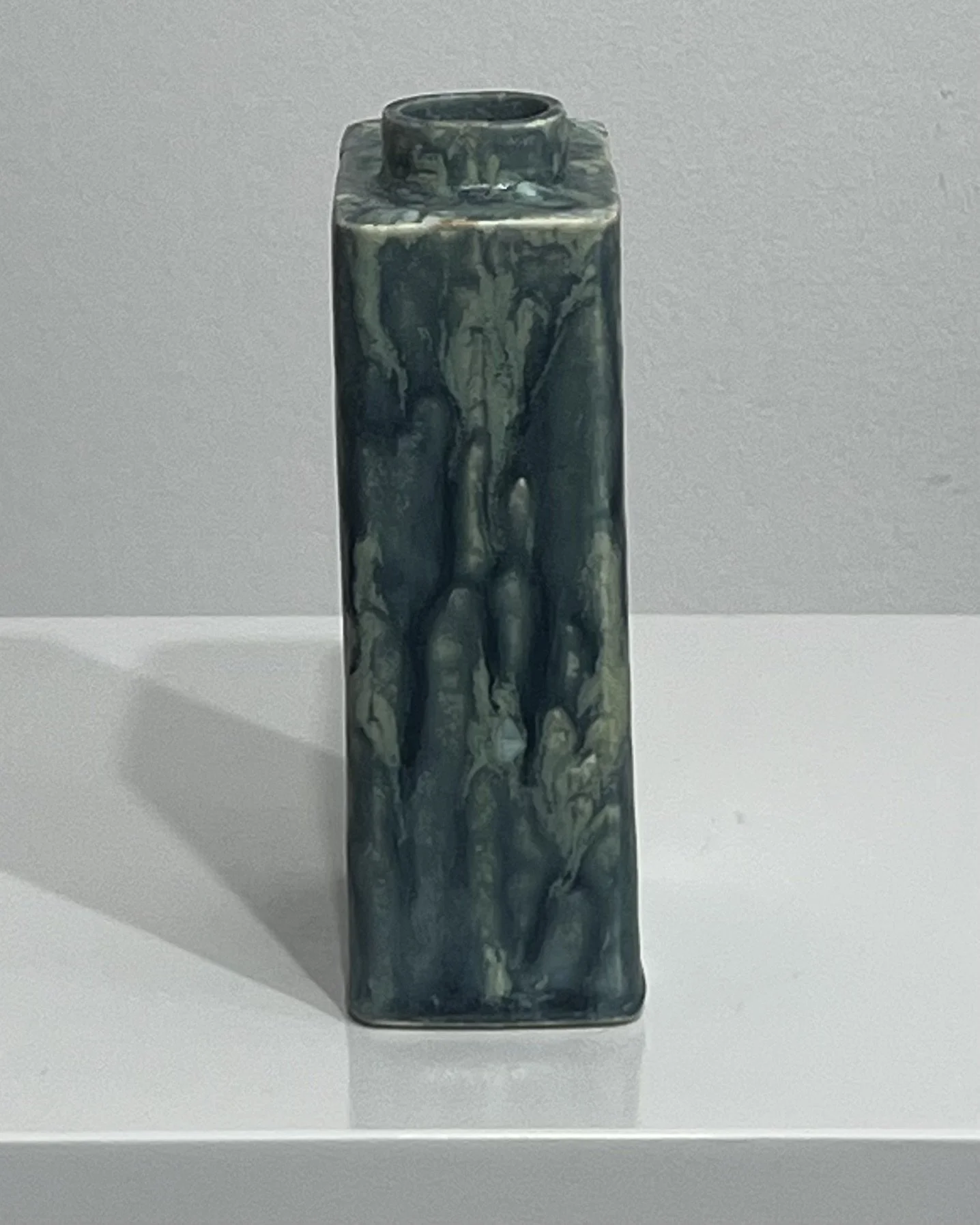 Left-side view of slim, angular handmade porcelain vessel with deep blue-green glazed surface.
