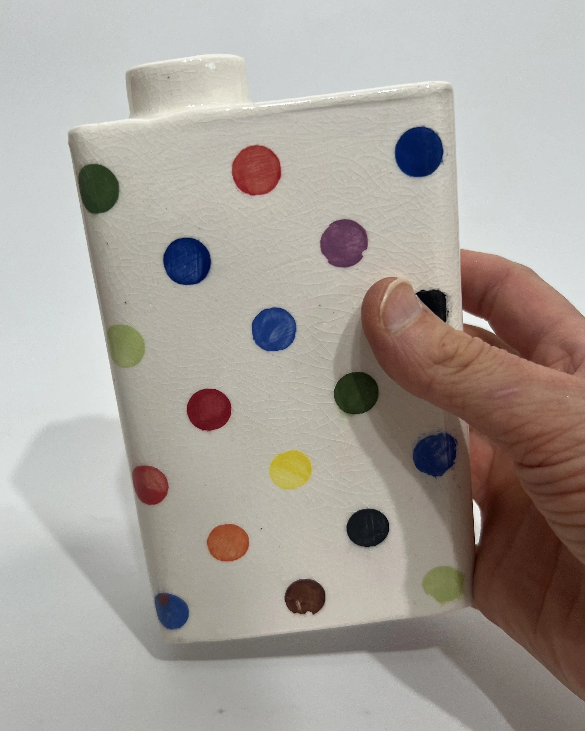 Hand holding multicolor polka dot carton vase to show scale
