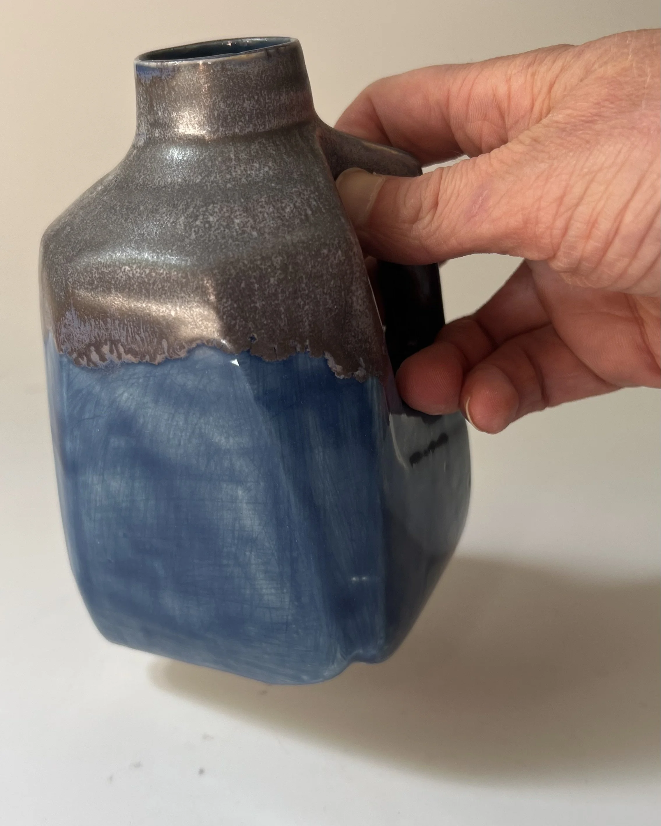Hand holding a handmade porcelain milk jug to show its scale and sculptural form.