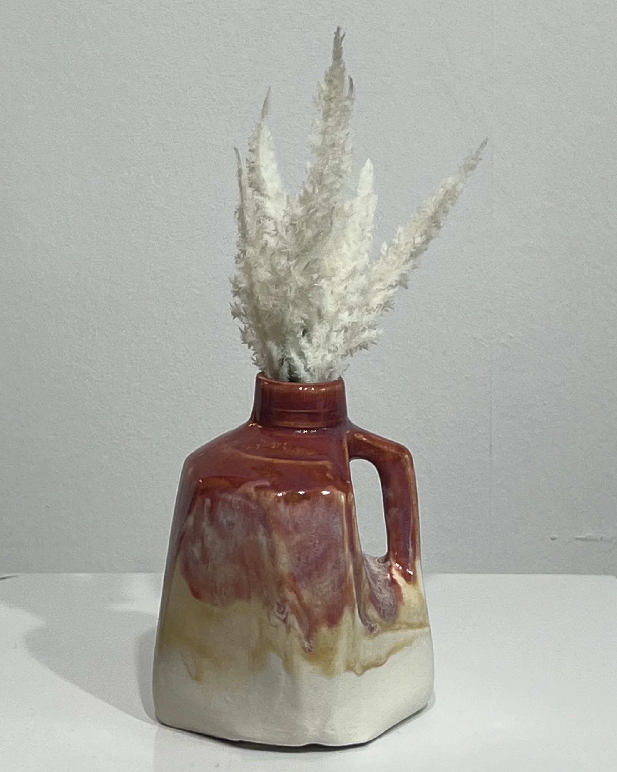 Handmade porcelain milk jug vase 26.80 by Alissa Van Atta, featuring burgundy Chun Plum and golden Honey Flux glazes flowing into an ivory base, styled with dried botanicals.