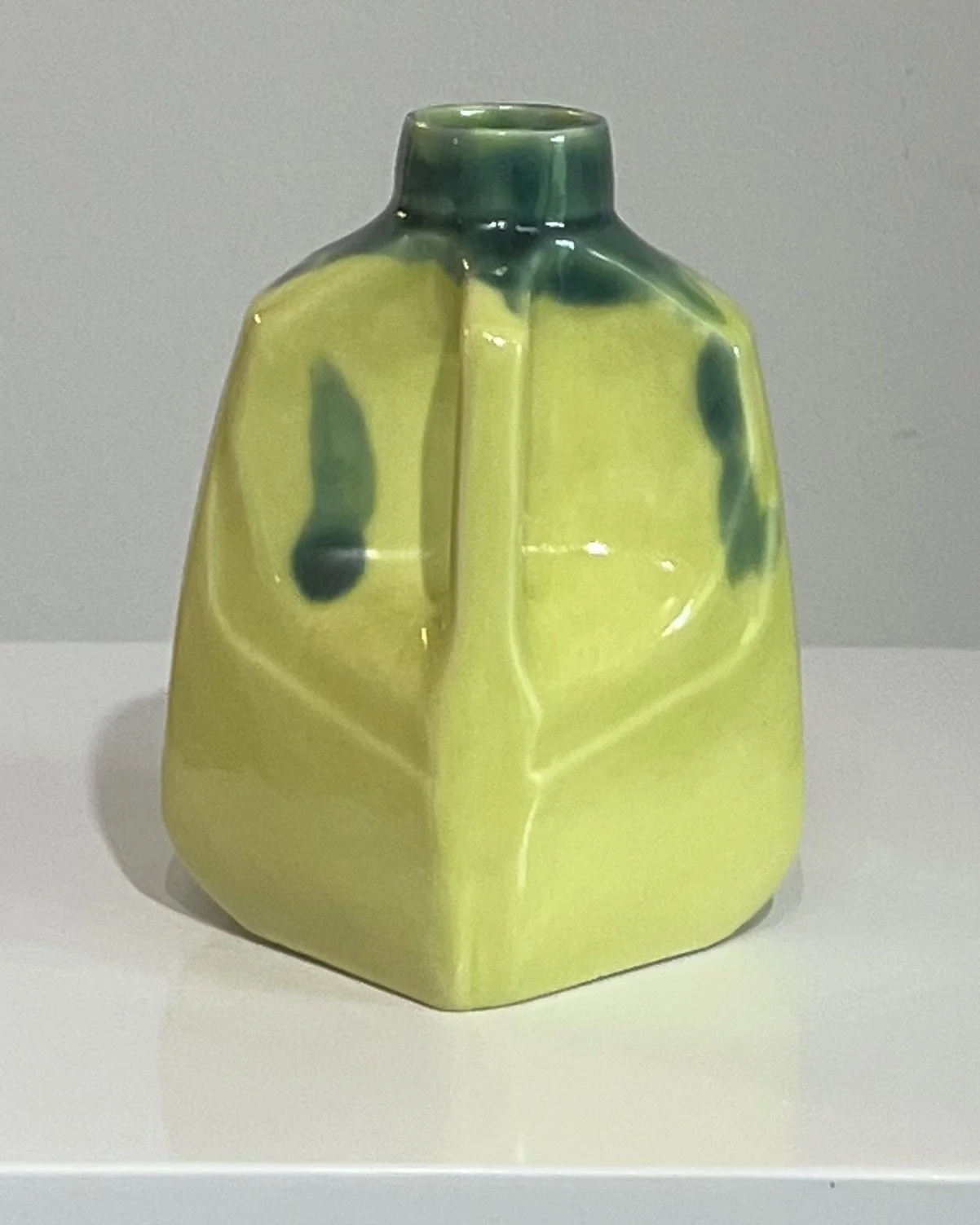 Side view of a one-of-a-kind porcelain milk jug with flowing lime green and dark green glazes.