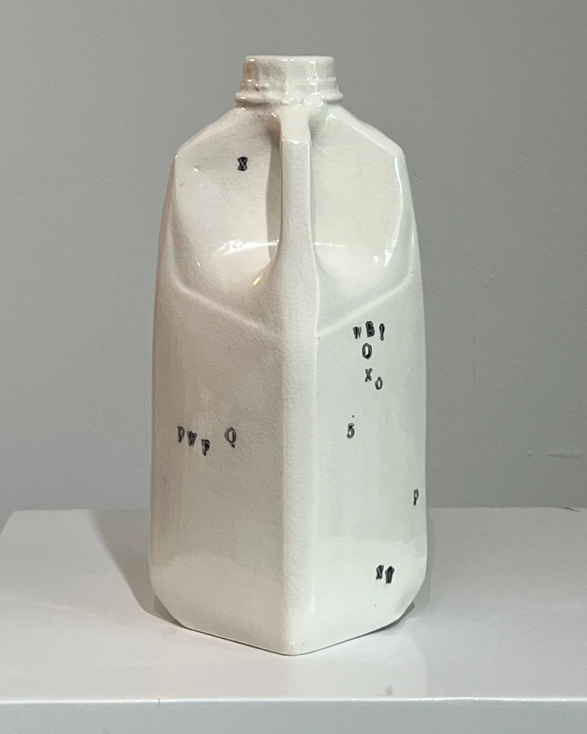 Angled right view of a tall white porcelain milk jug with hand-impressed typography and glossy finish.