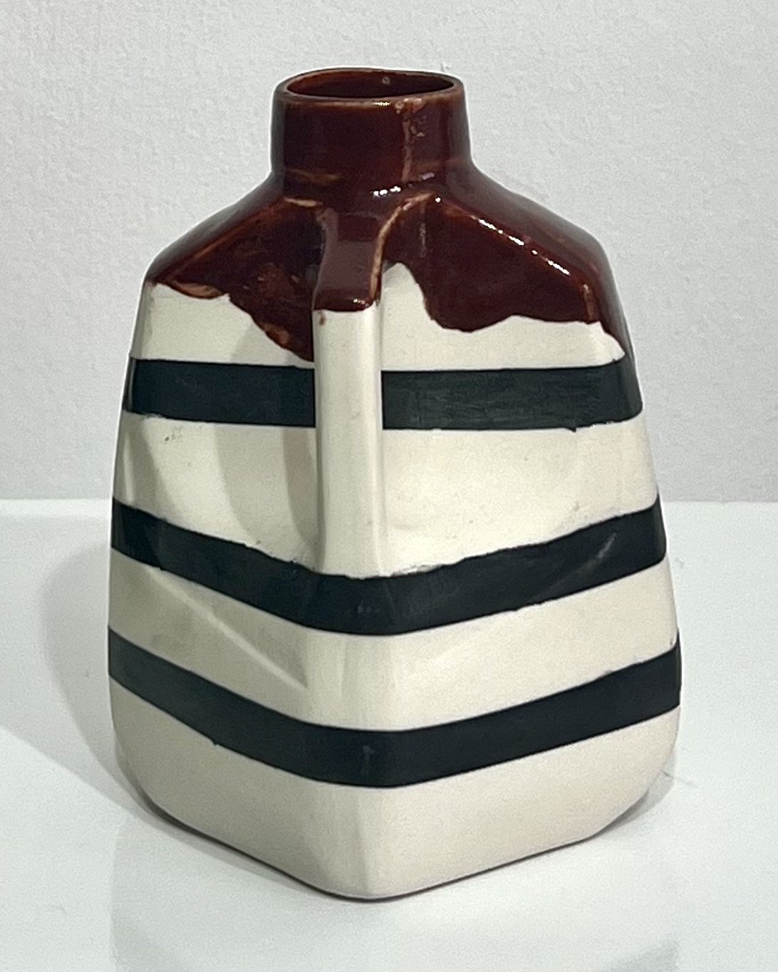 Porcelain milk jug No. 26.141 viewed with handle on the right, showing black painted stripes, a narrow neck, small spout, and glossy Deep Firebrick glaze.