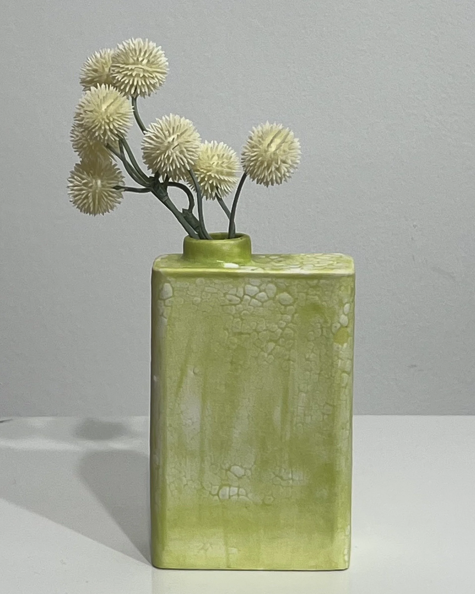 Handmade chartreuse porcelain Carton vessel by Alissa Van Atta displayed with small flowers.