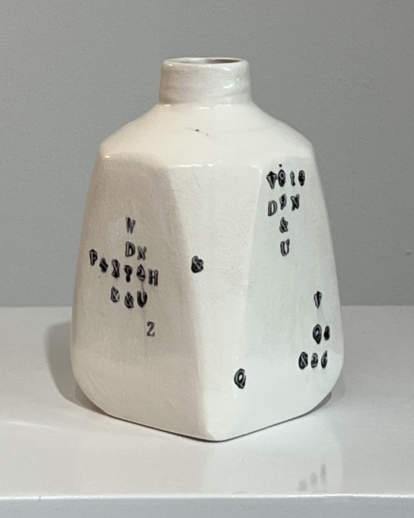 Angled left view of a contemporary handbuilt porcelain milk jug with impressed black typography and glossy white glaze.