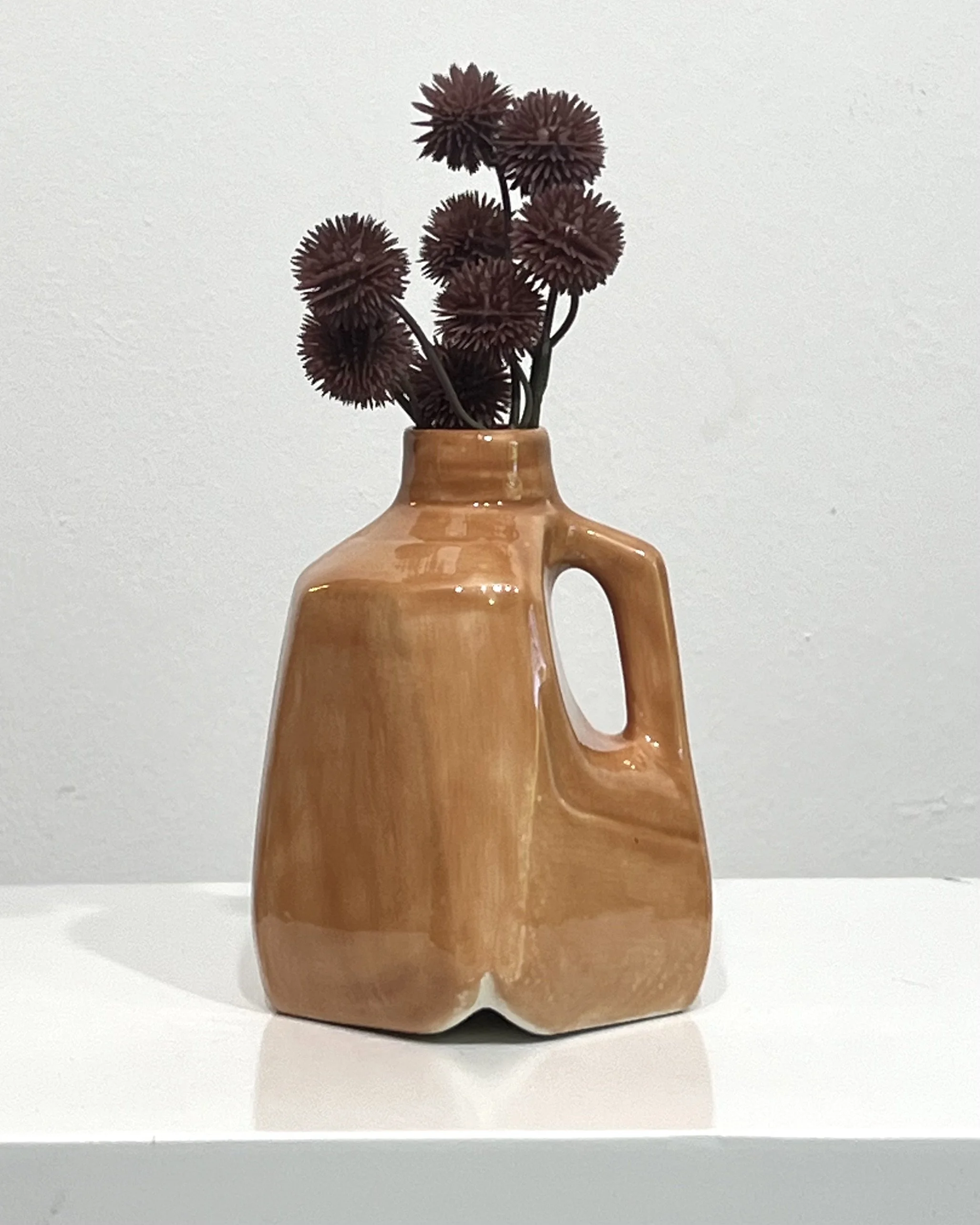 Porcelain milk jug vase in Sandalwood glaze displayed with burgundy dried flowers on a white pedestal.